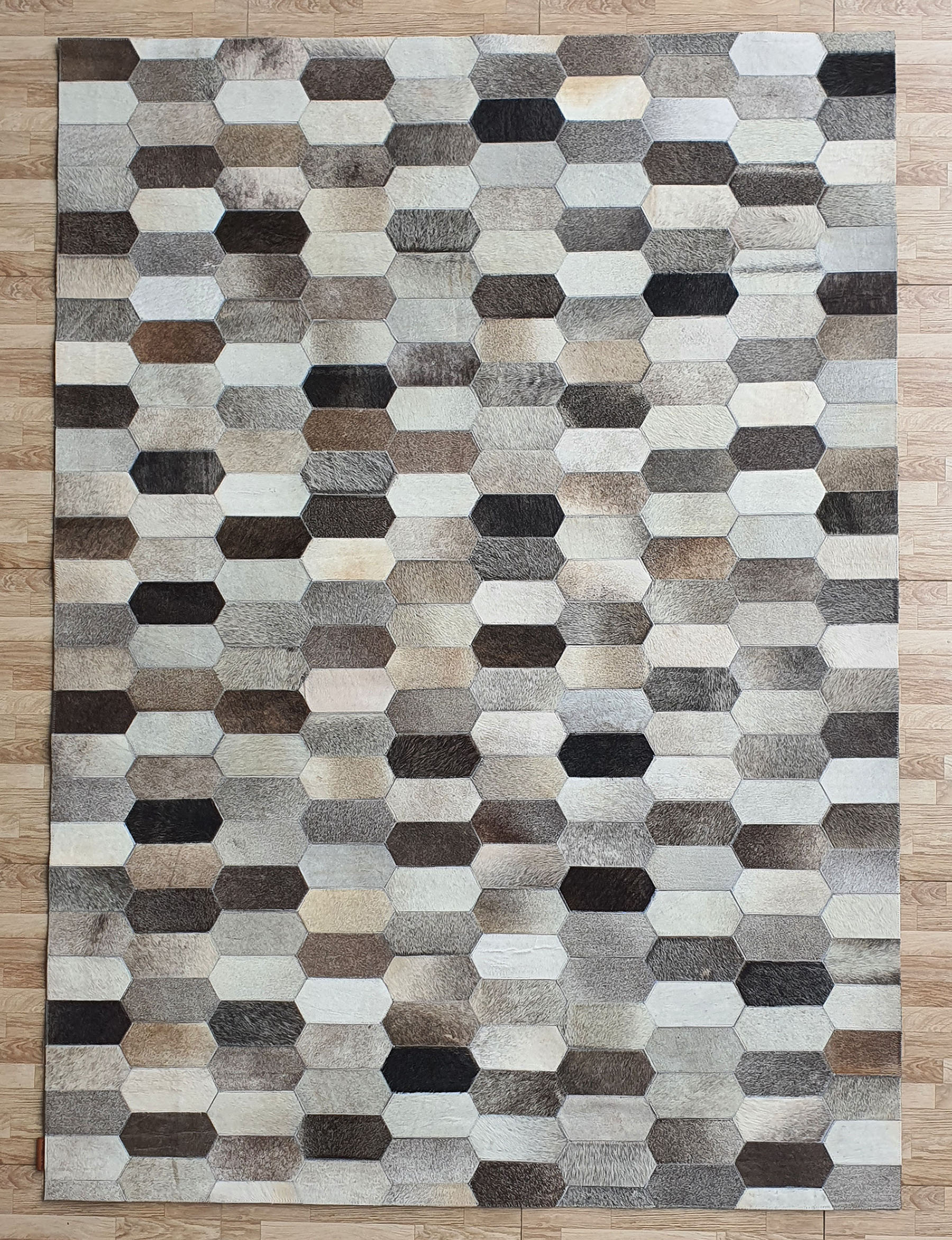 The RAMSHA HOME Multi Color Home Decor Leather Rug - LR 011 showcases a geometric hexagon pattern in gray, beige, and brown, elegantly displayed on a light wooden floor.
