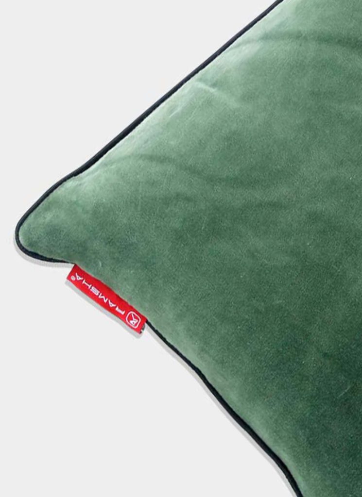 A close-up of the RAMSHA HOME Polyester Cushion Plain With Filler cs-233 in green velvet, with black piping and a red MAMBARA tag on one corner, set against a light background.