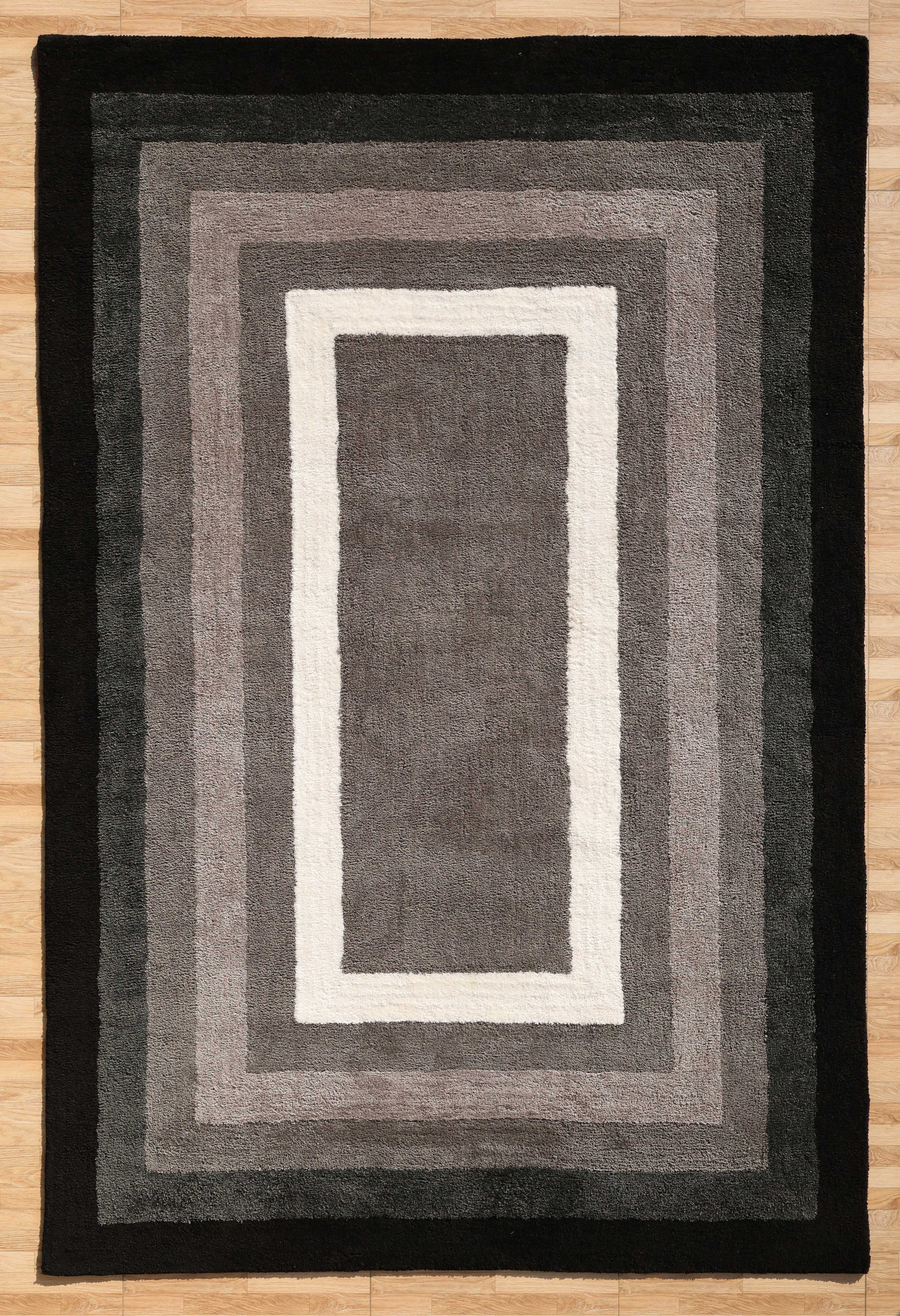 The RAMSHA HOME Black Shaggy Area Rug for Large Living Room - SG 049 features plush, concentric rectangles in gray, black, and white tones. Its soft texture and gradient design enhance comfort and depth on any light wooden floor.