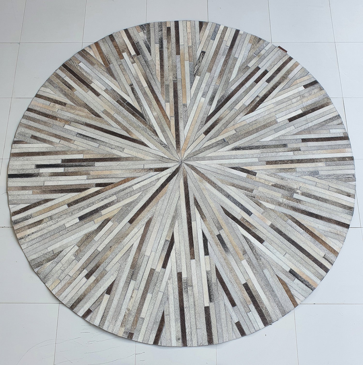 The RAMSHA HOME Home Decorative Leather Rug - LR 018 features a round starburst pattern in beige, brown, and gray strips, creating a stunning neutral look on a white tiled floor.