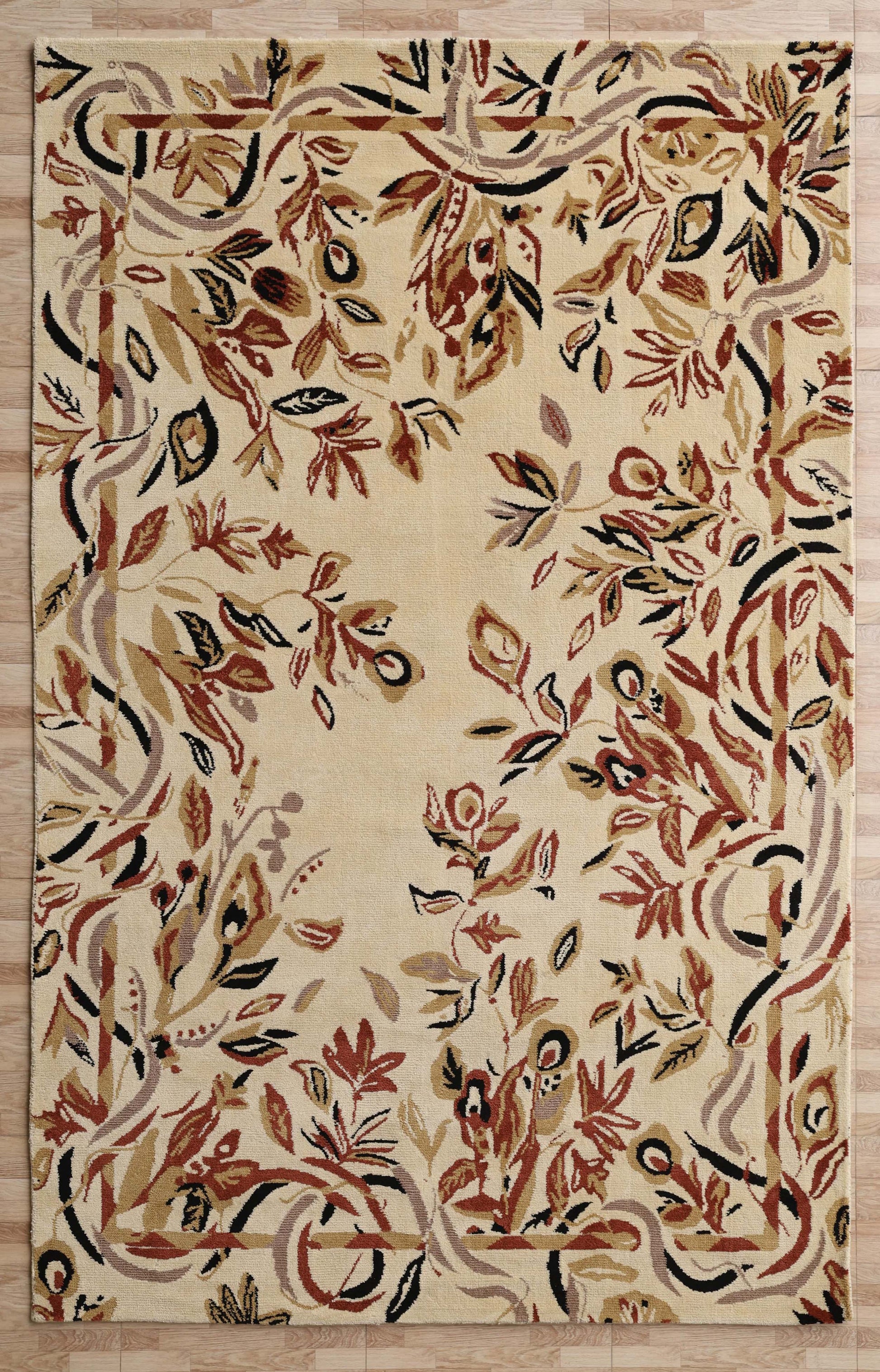 The RAMSHA HOME Vintage Floral Elegance Handmade Rug 200x300 CM -CMN 111 features a cream base with an abstract floral pattern in brown, red, tan, and black plus a wavy vine-like border. It is shown resting on a light wood floor.