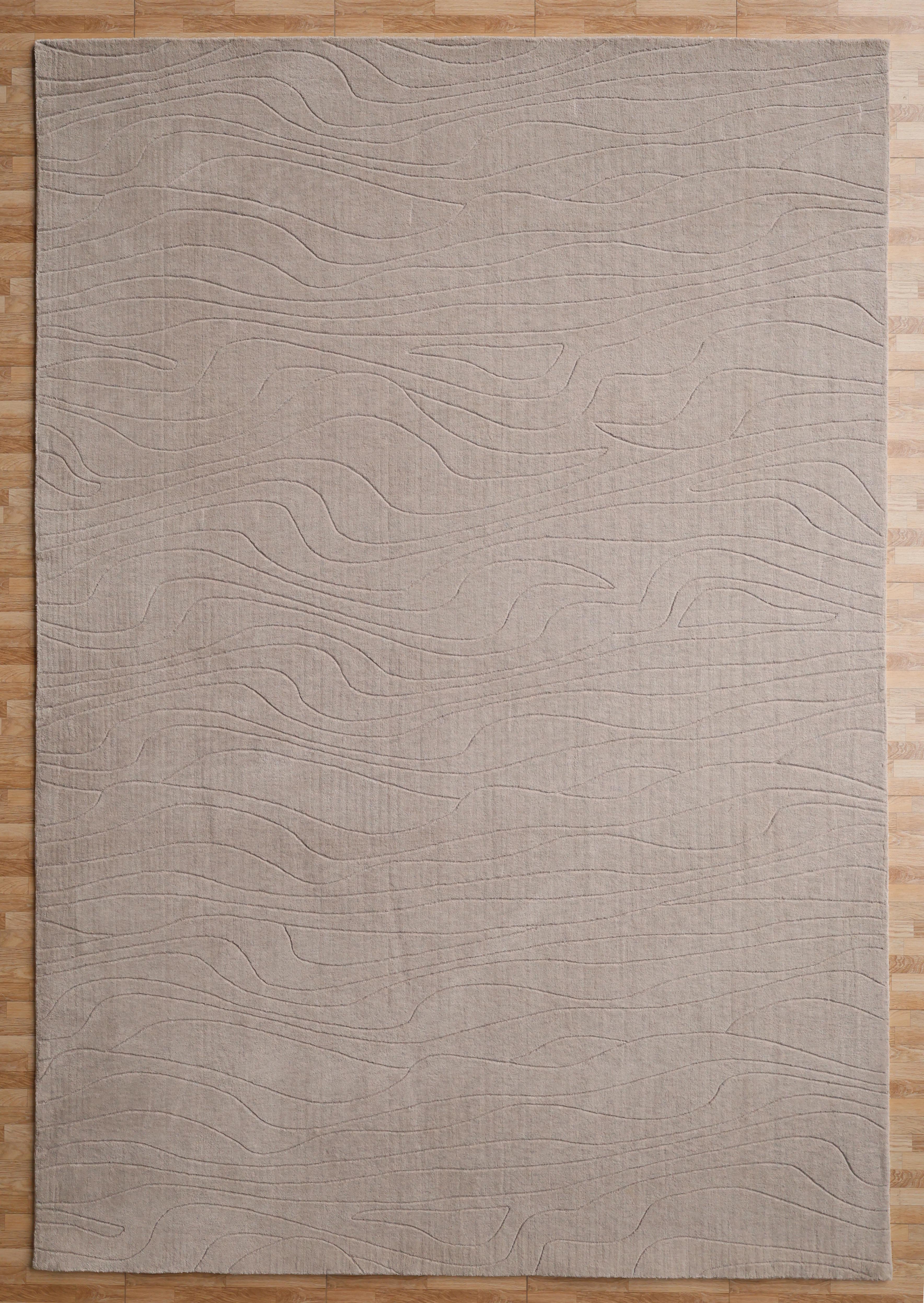 The RAMSHA HOME Light Grey Color Handmade 250x350 cm Area Rug (LKH-043) features a subtle wavy line pattern and is shown on a light wooden floor.