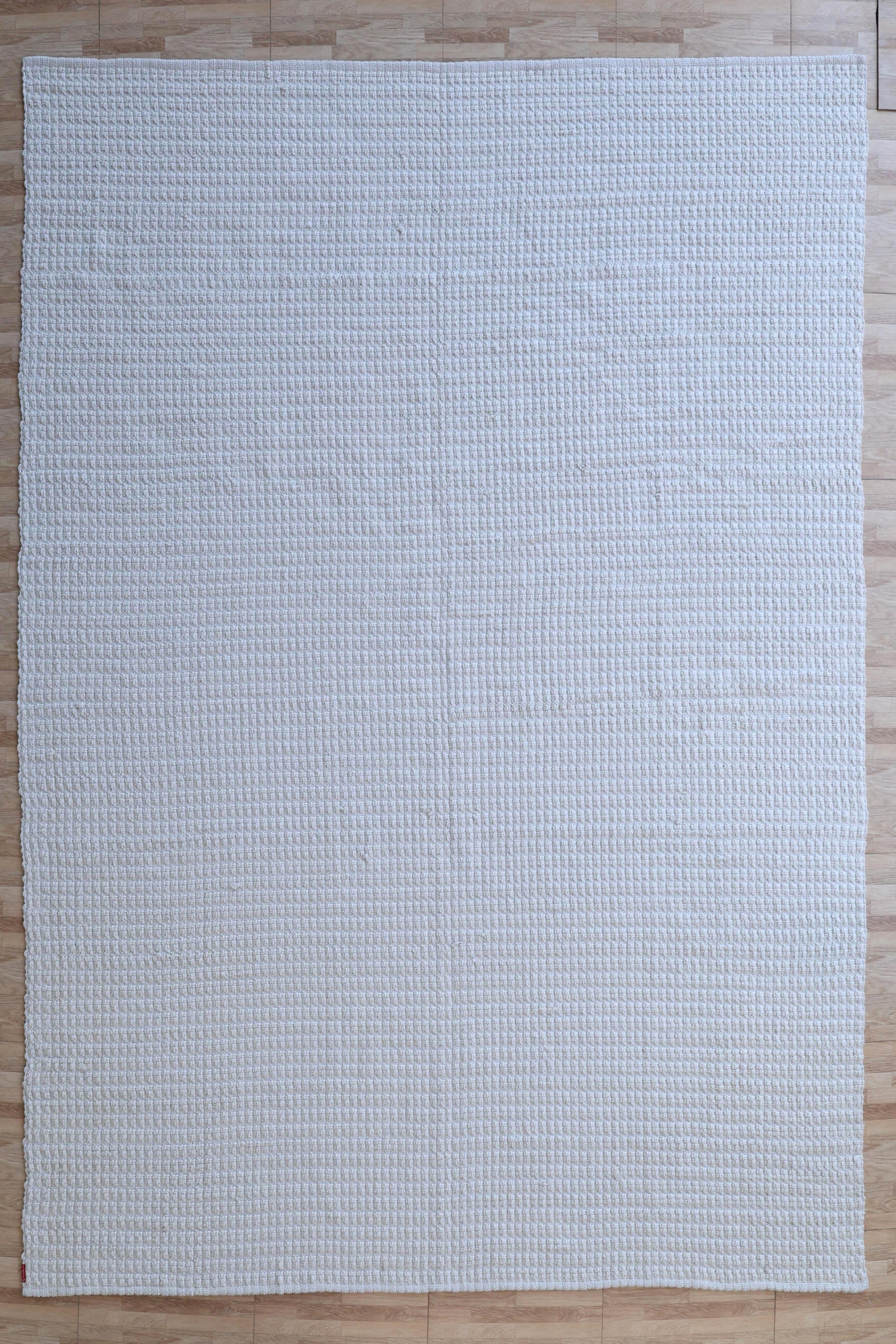 The Handmade Cream Natural Color Hand Woven Area Rug WR-039 by RAMSHA HOME, with its large rectangular shape and subtle textured grid pattern, adds artisanal charm and timeless elegance to any space when placed on a light wood floor.