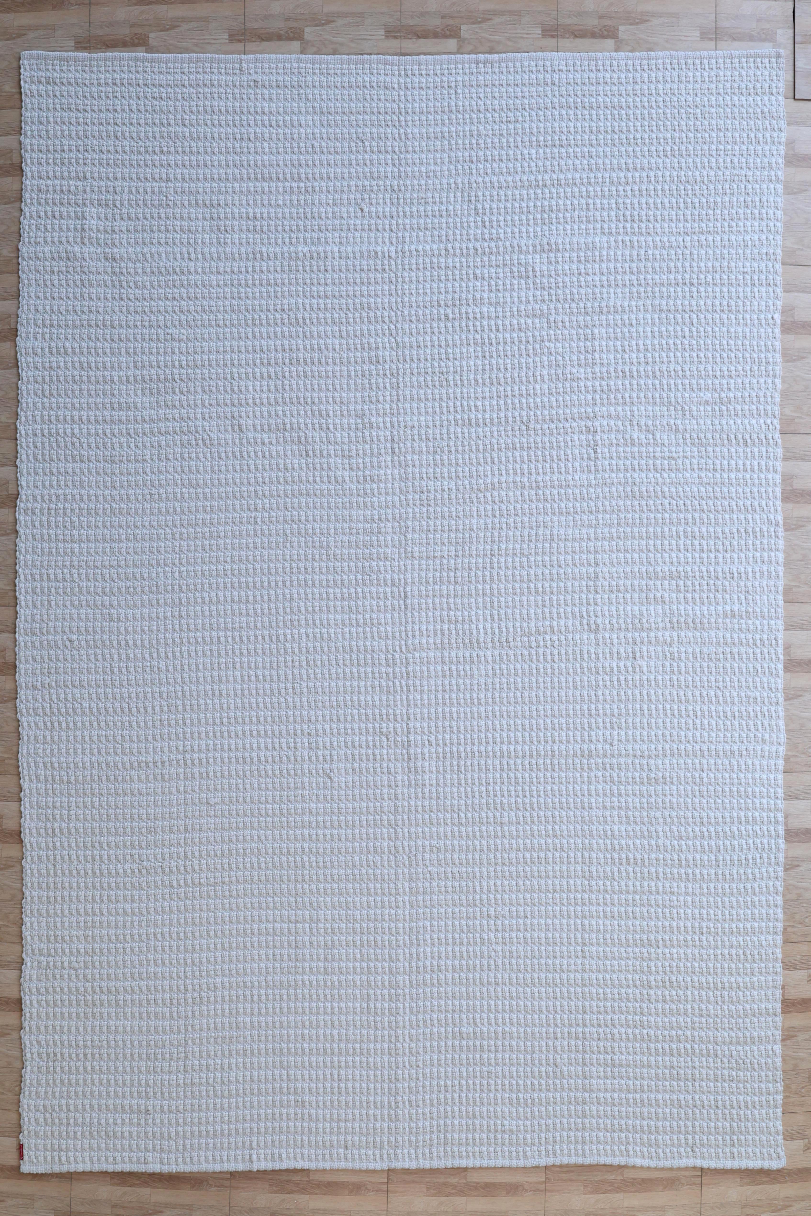 The Handmade Cream Natural Color Hand Woven Area Rug WR-039 by RAMSHA HOME, with its large rectangular shape and subtle textured grid pattern, adds artisanal charm and timeless elegance to any space when placed on a light wood floor.