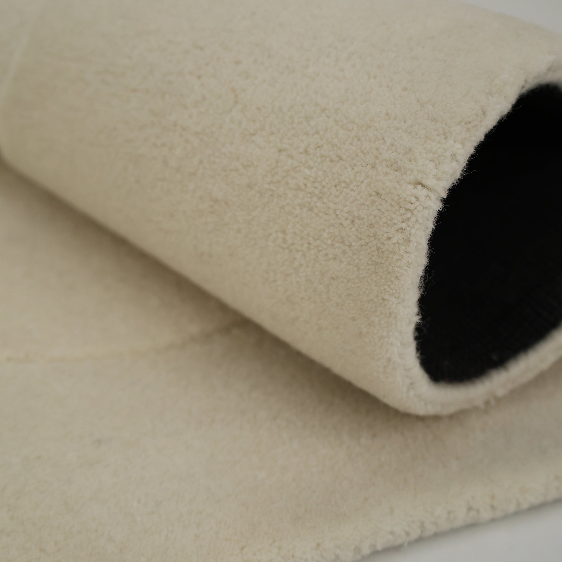 A close-up of the RAMSHA HOME Stylish Handmade Shape Rug Multi Color HTWV-105, rolled up to show its hand-tufted wool texture, soft fleece-like surface, and dark underside as it rests on a flat surface.