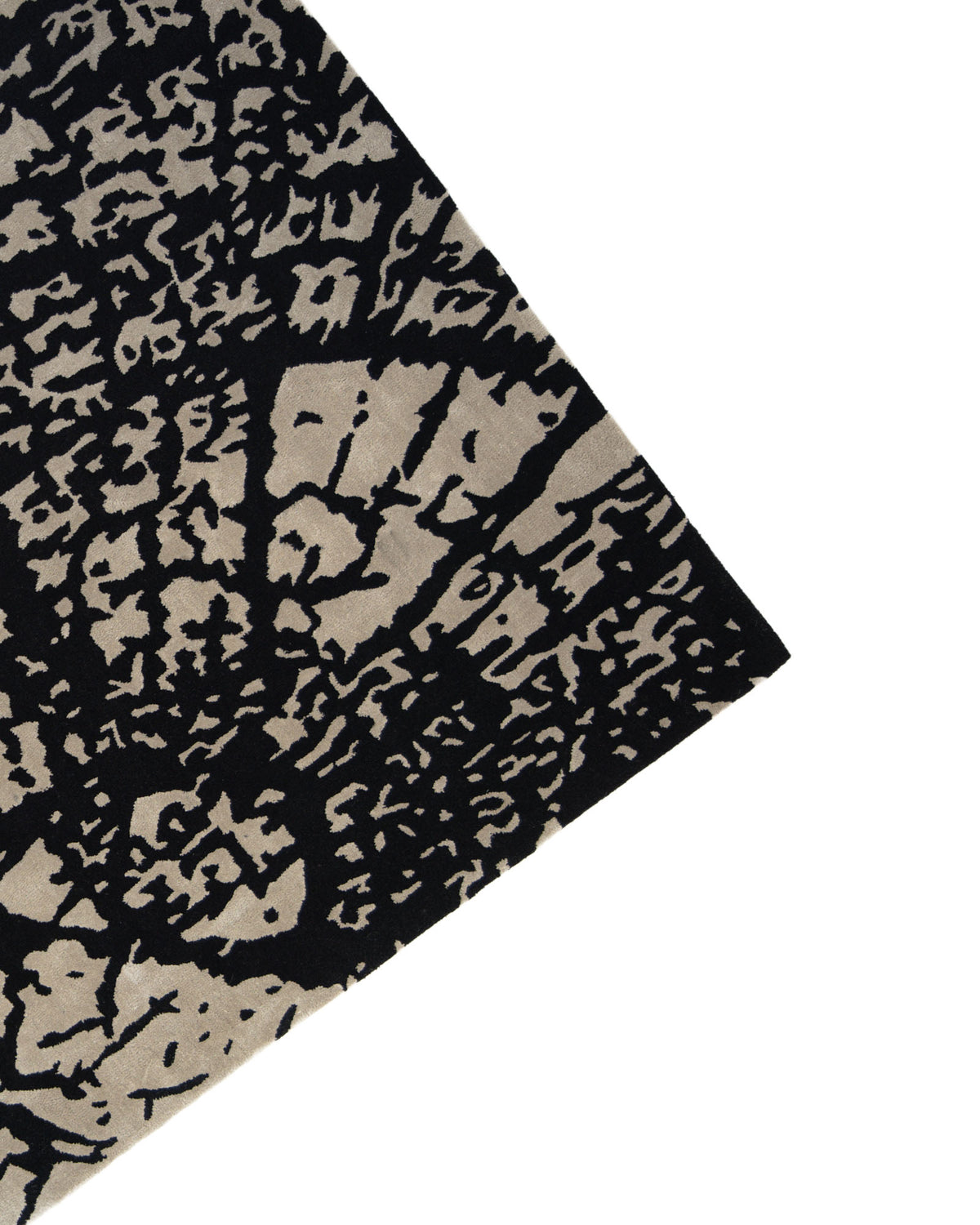 A close-up of the RAMSHA HOME Abstract Crackle Black & Ivory Rug – HTWV-33, highlighting its hand-tufted corner with a striking black and gray cracked pattern on a white background, showcases the luxurious texture and modern style of this black and ivory rug.