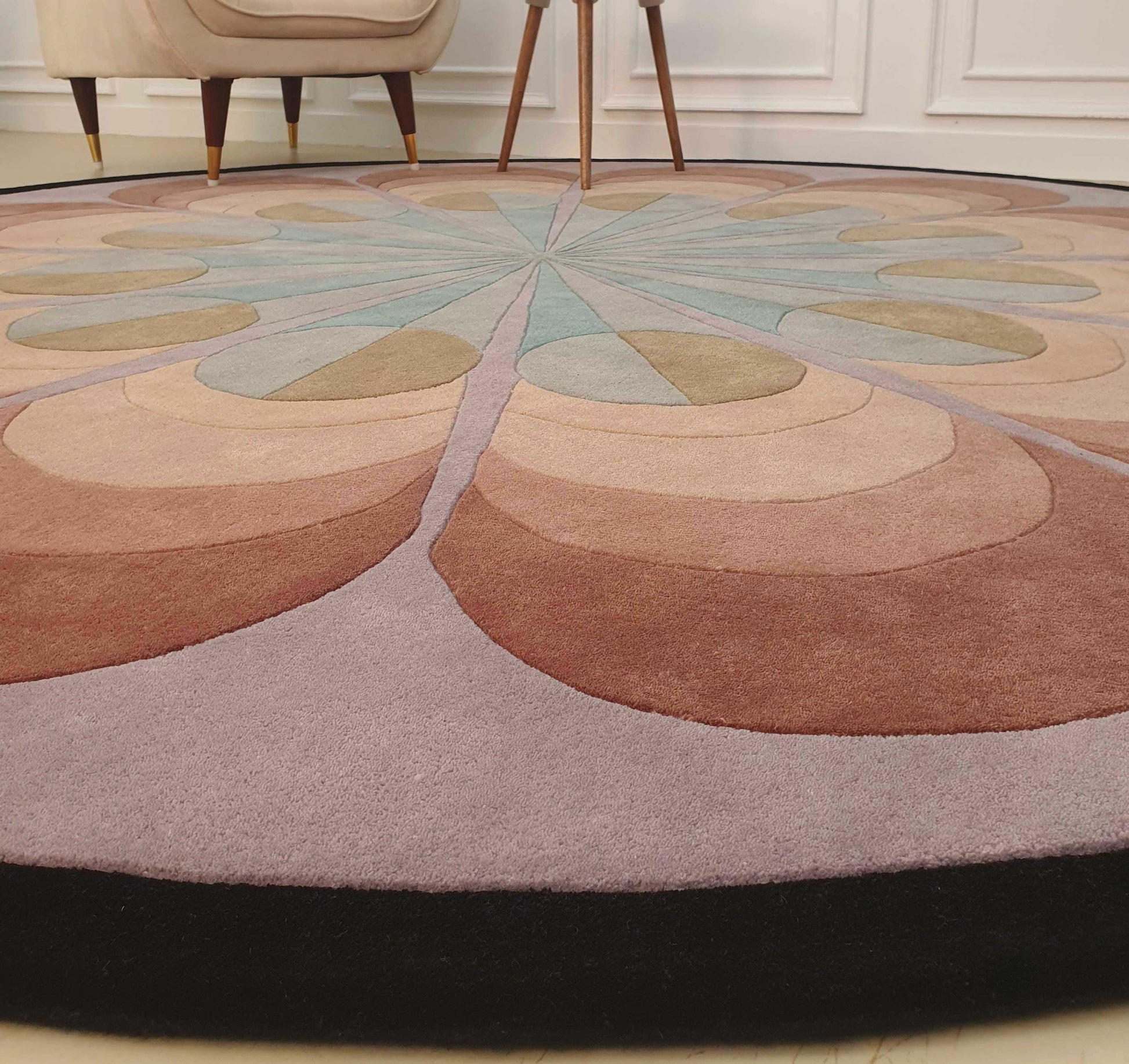 The RAMSHA HOME Handmade Carpet for Bedroom Decor – HTW-54 is a round wool rug featuring a geometric, petal-like pattern in brown, beige, mauve, and light blue. This hand-tufted rug adds elegance to any room decor.
