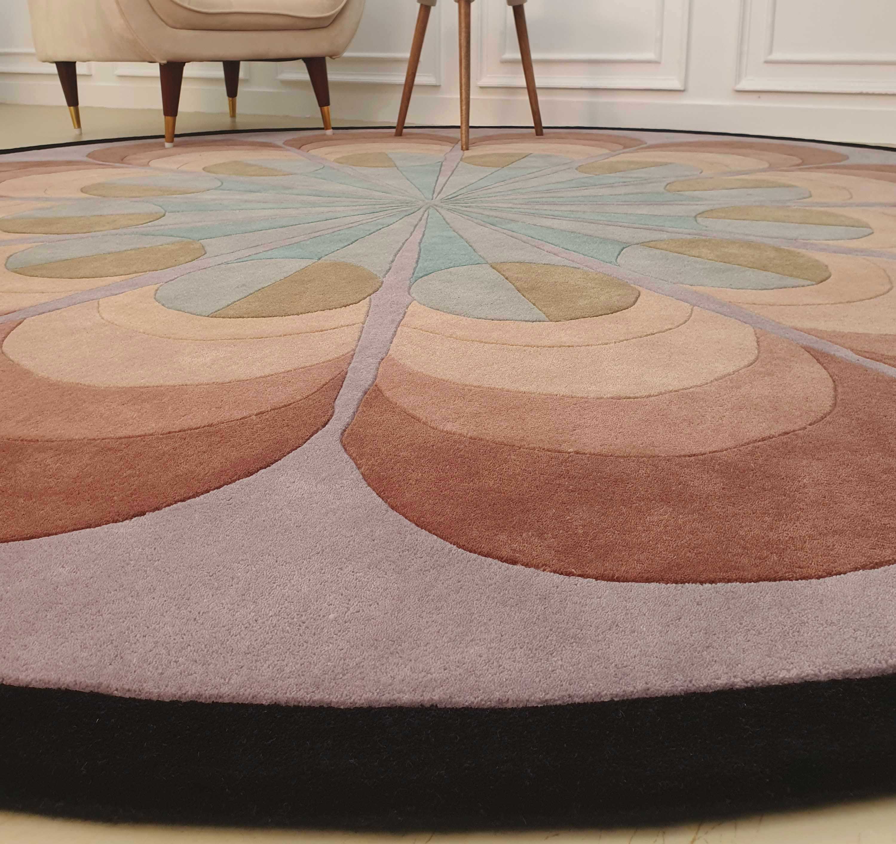 The RAMSHA HOME Handmade Carpet for Bedroom Decor – HTW-54 is a round wool rug featuring a geometric, petal-like pattern in brown, beige, mauve, and light blue. This hand-tufted rug adds elegance to any room decor.