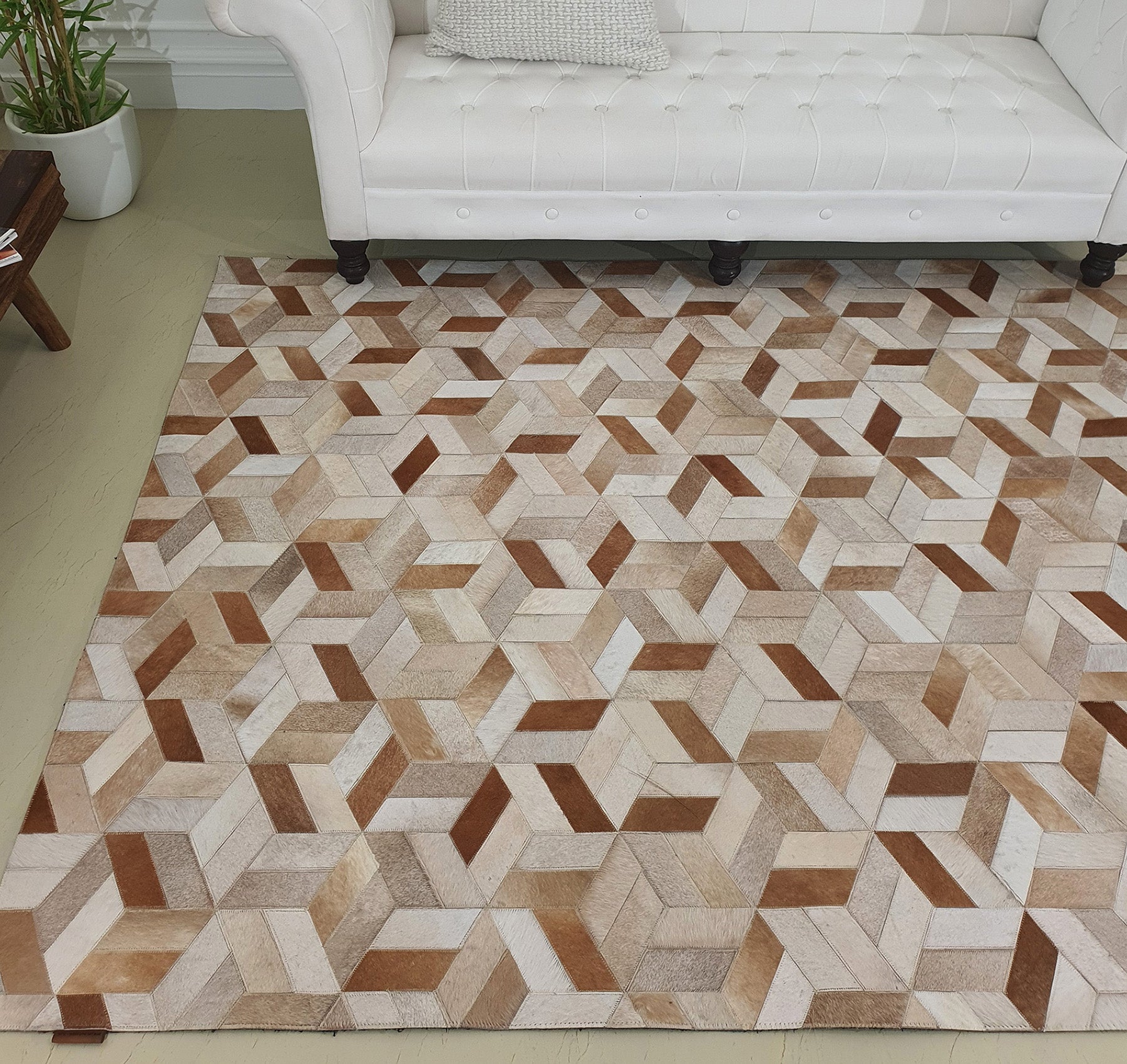The RAMSHA HOME Geometric Cube Pattern Handmade Leather Area Rug LR-012, featuring a 3D cube design in beige, brown, and tan, enhances the modern look of the room placed before a white tufted sofa on a light floor.