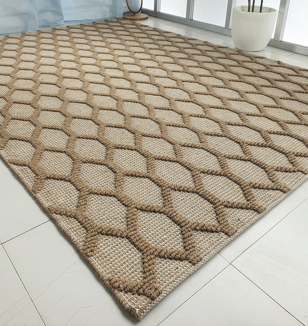 The RAMSHA HOME Rectangle Woven Area Rug Neutral Beige And Brown SR-023 features a raised honeycomb pattern, placed on a light tiled floor near a large window and a white potted plant.