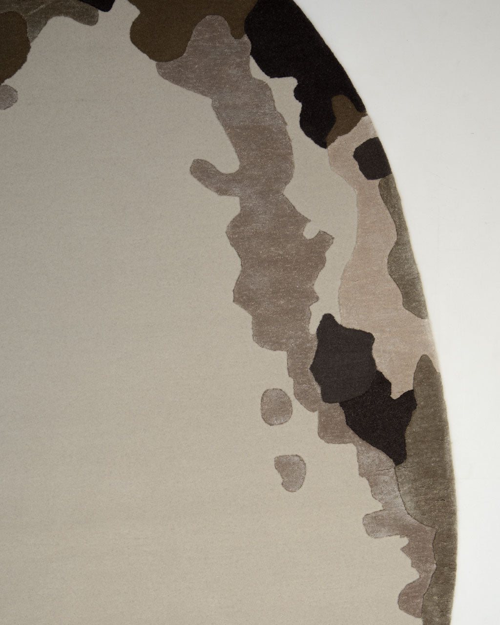 Introducing the Terra Eclipse Oval Handmade Rug Accent Rug HTWV-195 by RAMSHA HOME—an abstract contemporary rug with an earth-toned camouflage pattern along the edge, showcasing beige, brown, tan, and black shapes on a light background. This handmade rug curves its unique design from the top left to the bottom right, making it a striking addition to any space.