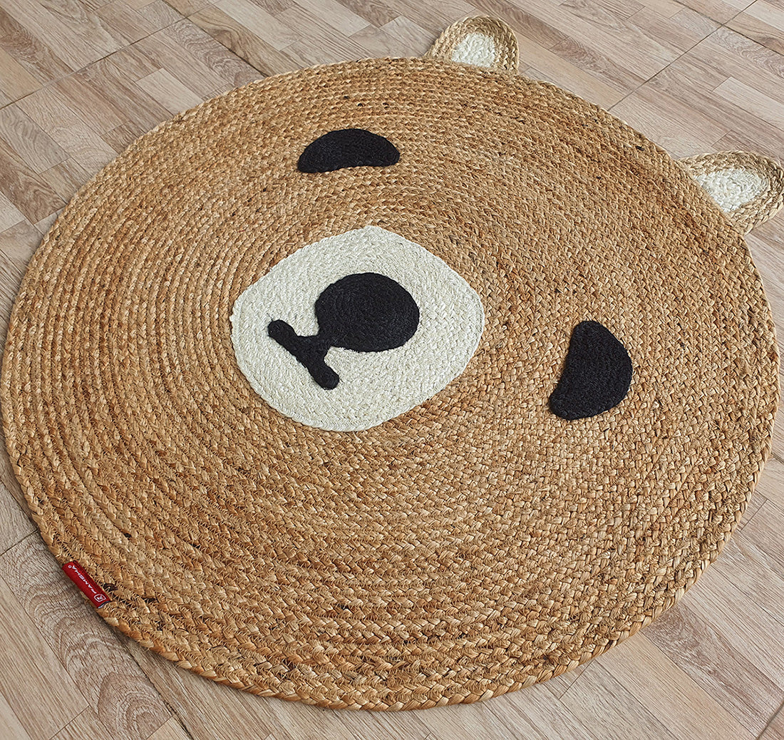 The Amazing Handmade Bear Shape Jute Rug - BR 022 (90cm) by RAMSHA HOME features a round bear face with black eyes, beige snout, and ears, adding playful charm, cozy warmth, and character to any wooden floor.