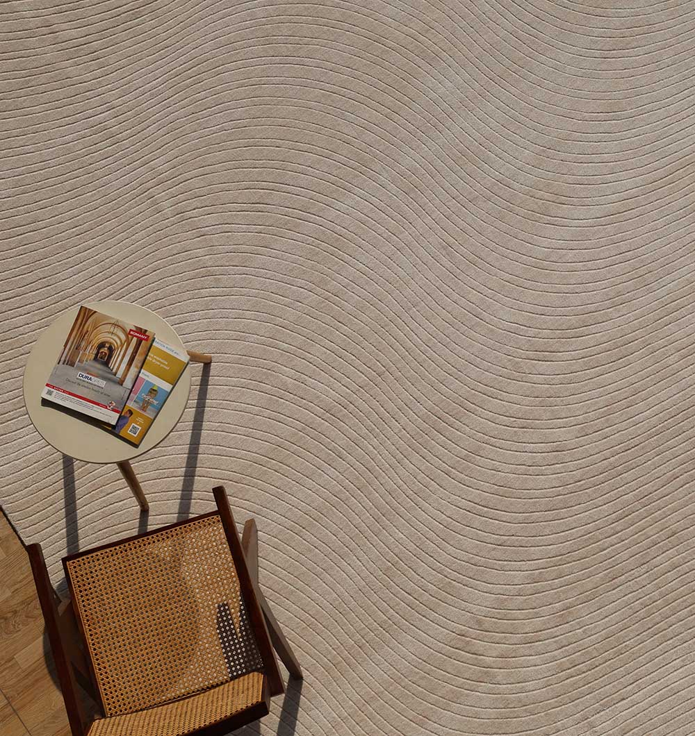 A small round table with magazines and a cane chair sit on the RAMSHA HOME Natural Handmade Area Rug - LKH-03 (300x400 cm), featuring beige textured curves for a minimalist, serene look.
