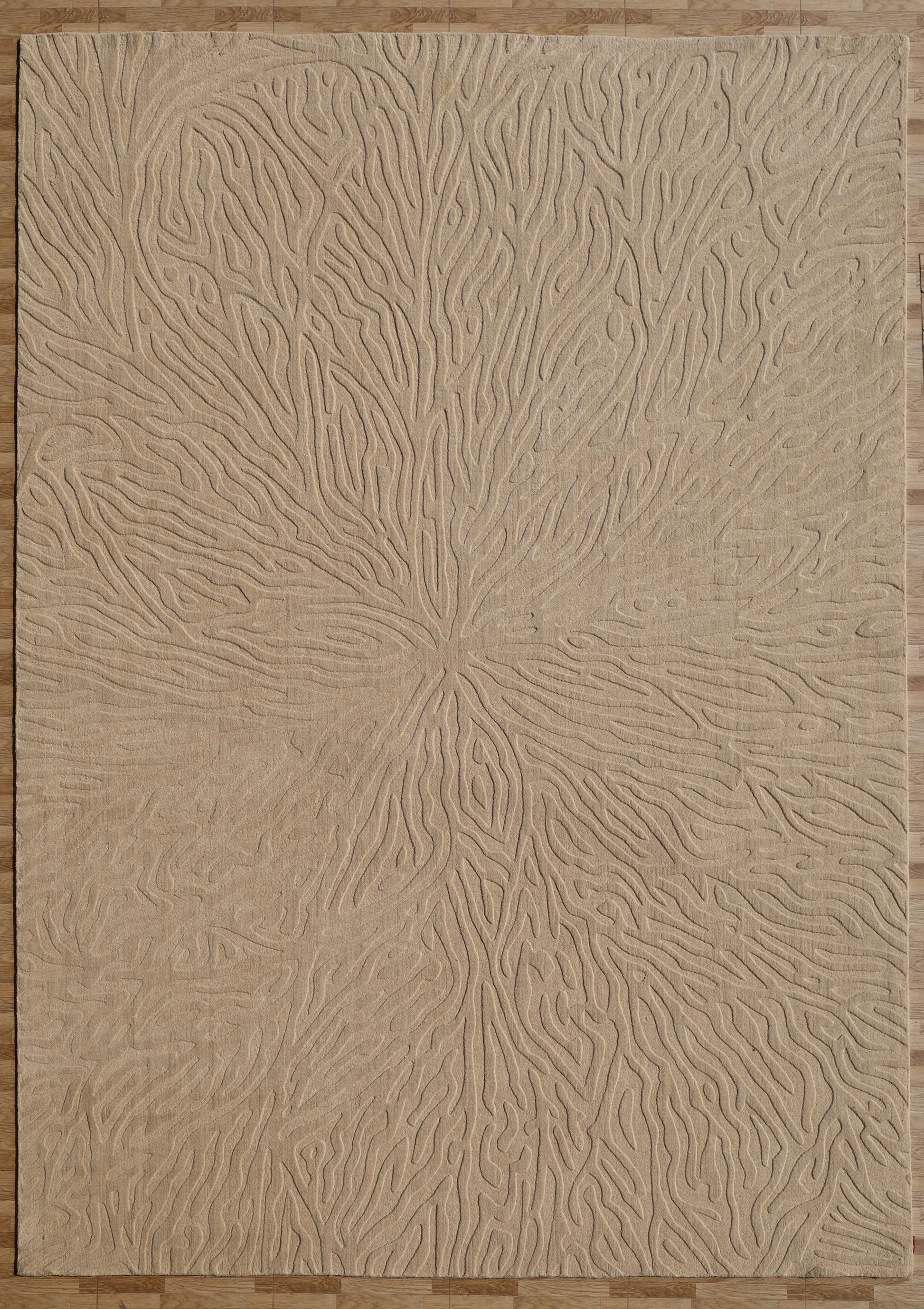 A Handmade Beige Rug with Organic Tree-Inspired Pattern (LKH-025) by RAMSHA HOME lies on a wooden floor, showcasing its intricate embossed high-low design of raised, wavy lines that radiate outward like tree rings or flowing water.