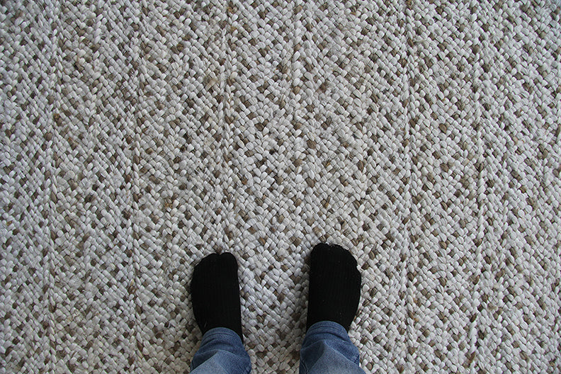 A person in black socks and blue jeans stands on the RAMSHA HOME Handmade Natural & White Crochet Rug (CR 004, 200x300cm), viewed from above.