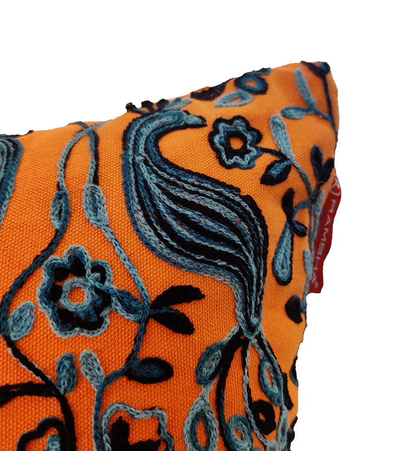 Close-up of the Multi Color Flower Embroidery Cushion CS-268 by RAMSHA HOME, featuring vibrant blue and black floral and peacock embroidery, with a small red fabric tag. Set against a plain white background.
