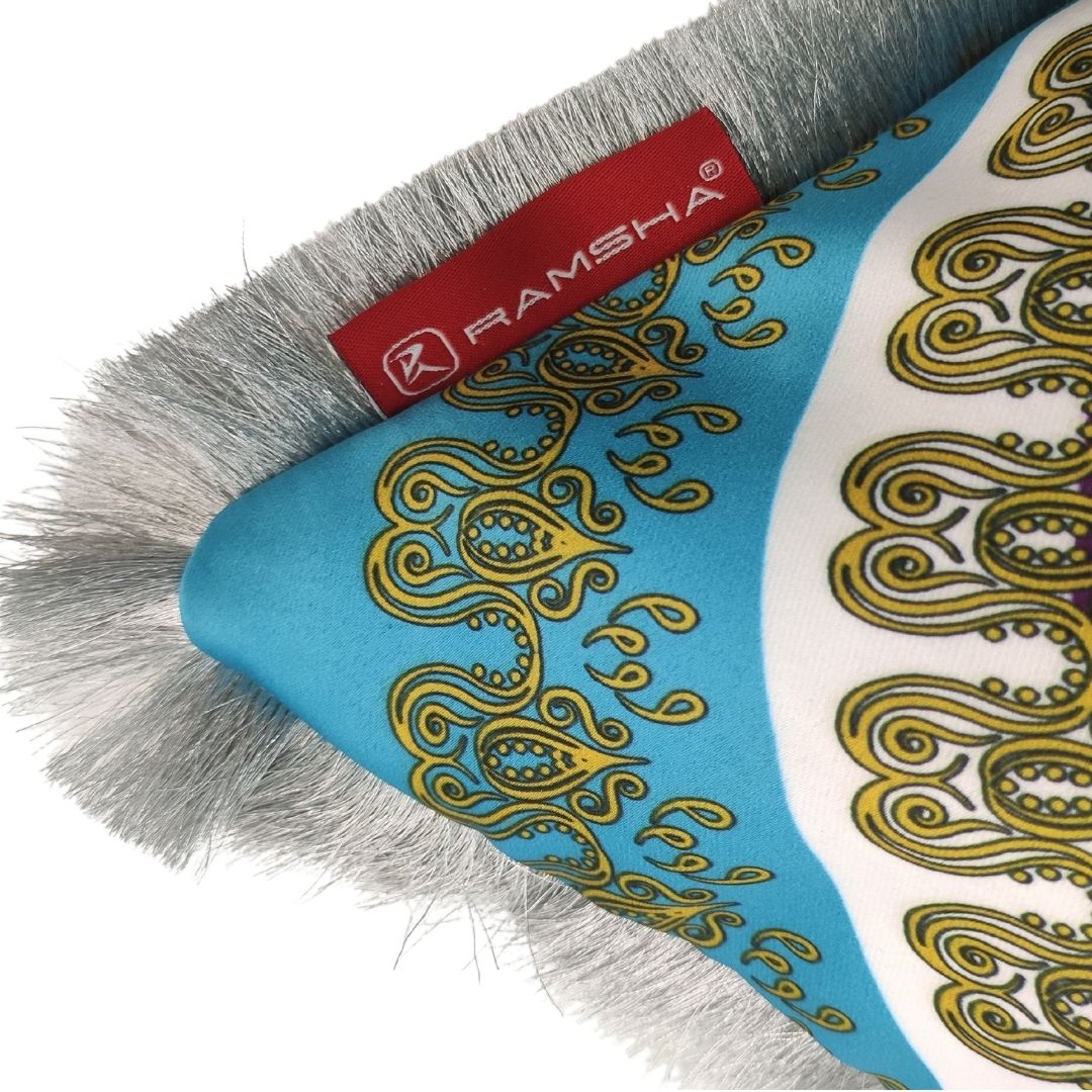 A close-up of the premium "Polyester Multi Cushion With Filler CS-063" by RAMSHA HOME, featuring a blue and gold pattern, grey fur trim, and a red fabric tag with the RAMSHA® logo.
