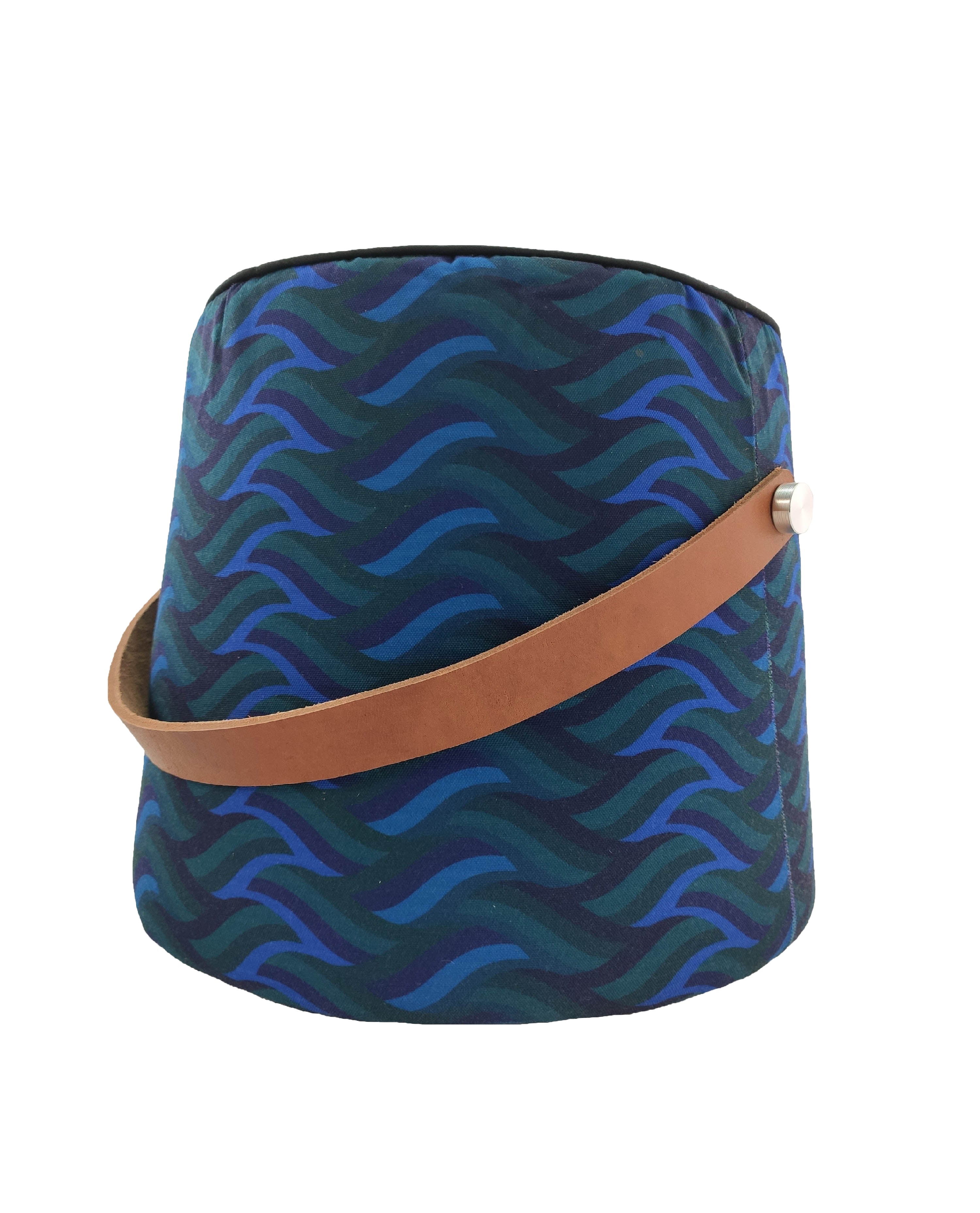 The RAMSHA HOME Blue Printed Pedestal Pouf With Leather Handle PF-037 features a blue and teal wavy design with a brown leather handle attached by a metal stud—ideal for adding style to your home decor.