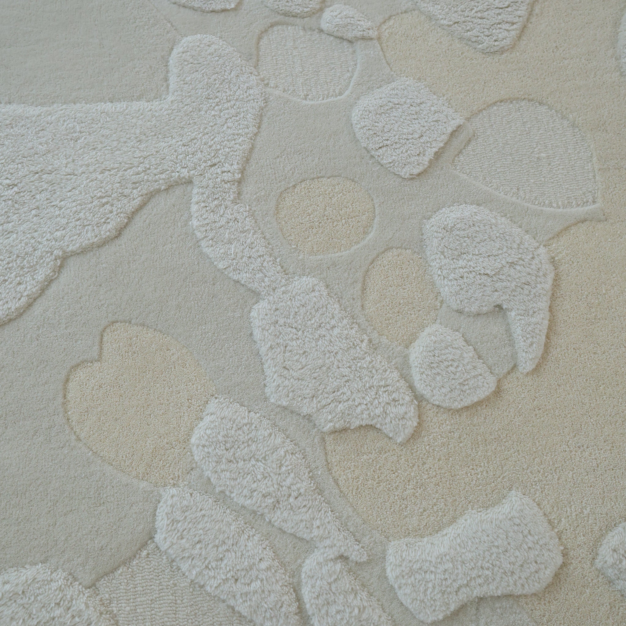 A close-up of the RAMSHA HOME Creative Multi Color Wool & Cotton Handmade Rug - HTW 69 (200x300cm) shows neutral abstract shapes in cream and beige, with raised and flat areas for a sculpted look that adds tactile depth to any room.