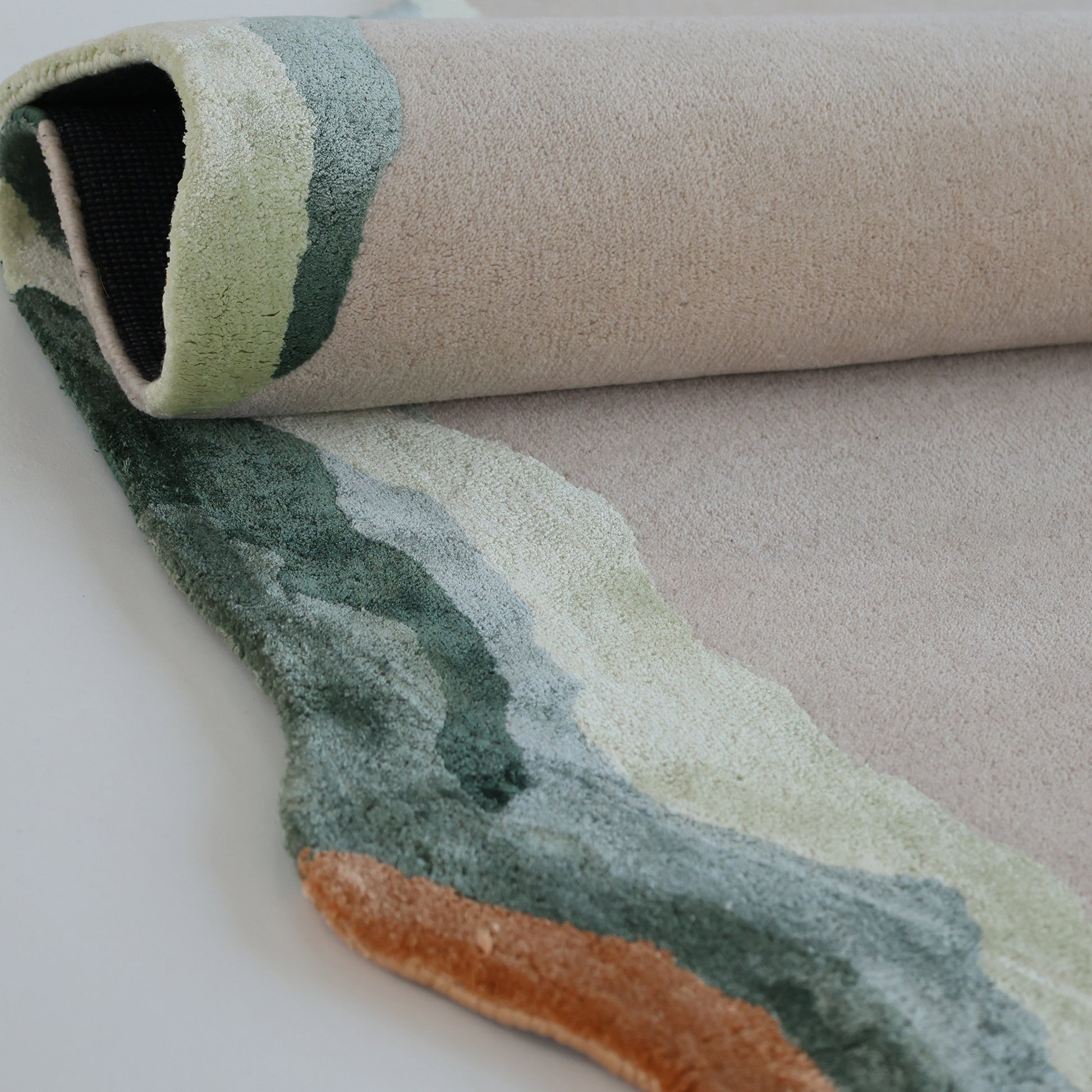 A close-up of the RAMSHA HOME Handmade Decorative Multi Color Rug HTWV-92 shows its hand-tufted, irregular edges and layered beige, green, light blue, and orange patterns. This modern wool rug has a soft, textured look.