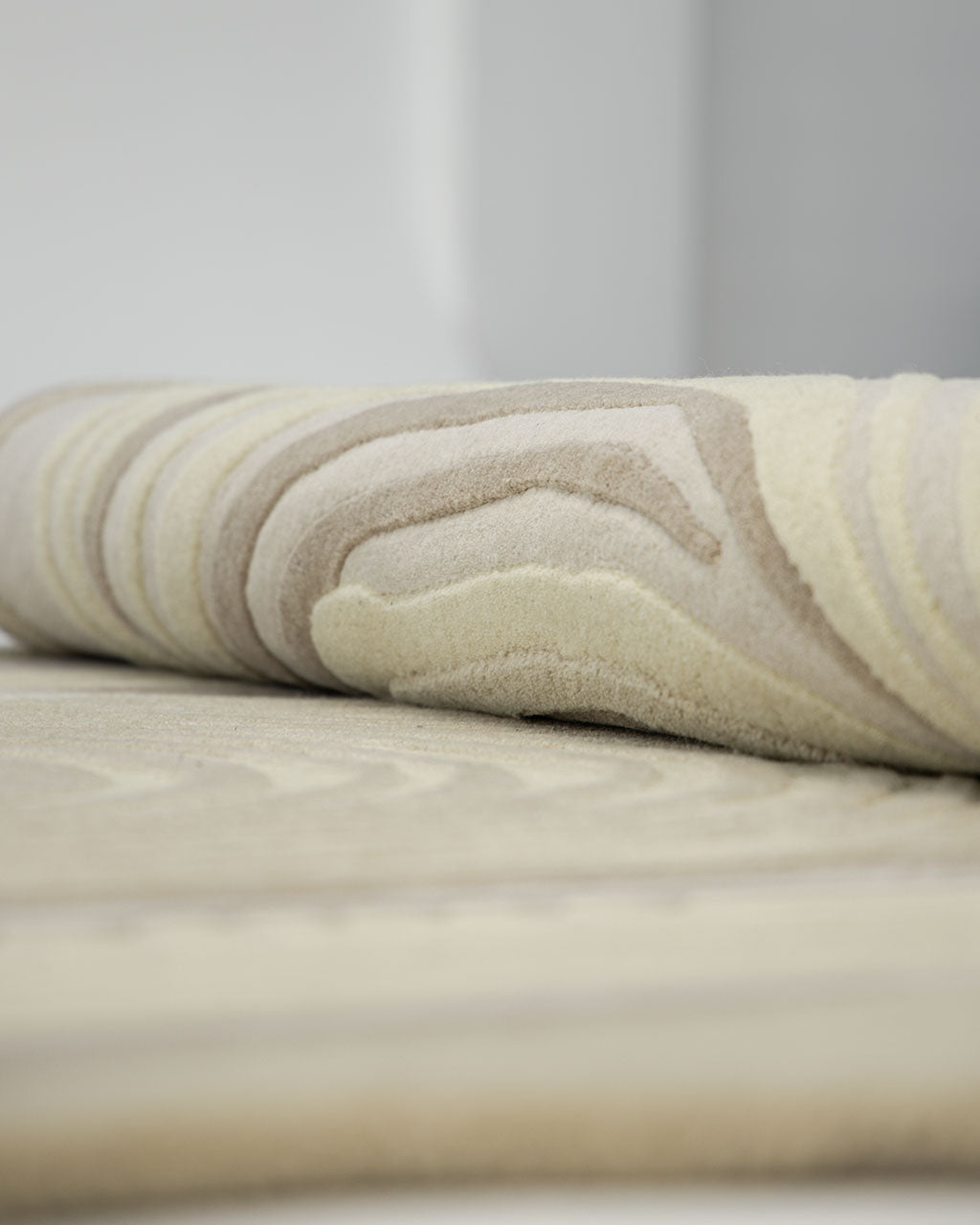 Close-up of the RAMSHA HOME Terra Eclipse Oval Handmade Rug Accent Rug HTW-155, rolled to showcase its beige and cream hues with a raised, wavy textured pattern. The soft surface and subtle color variations are clearly visible.