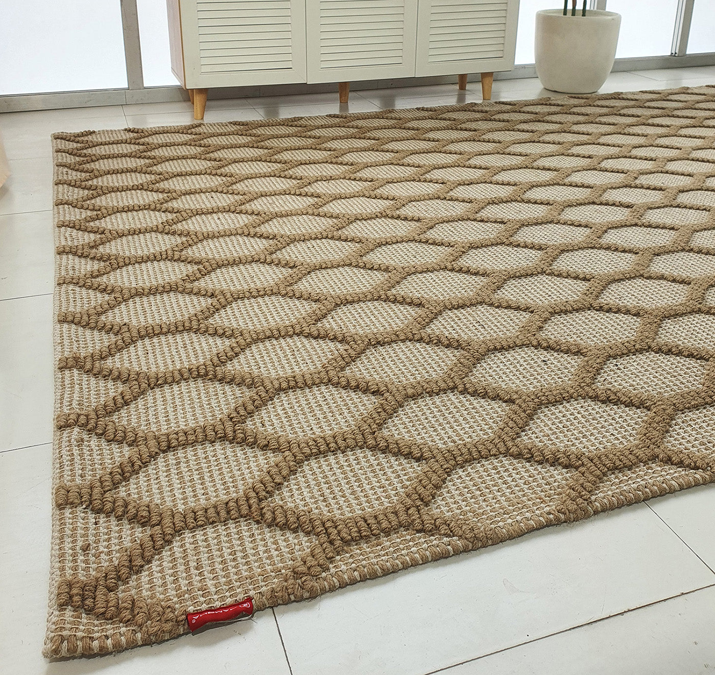 The RAMSHA HOME Rectangle Woven Area Rug Neutral Beige And Brown SR-023 with a diamond lattice design is laid on light tiles in a modern room with white furniture and a potted plant. A small red tag accents this elegant rug.