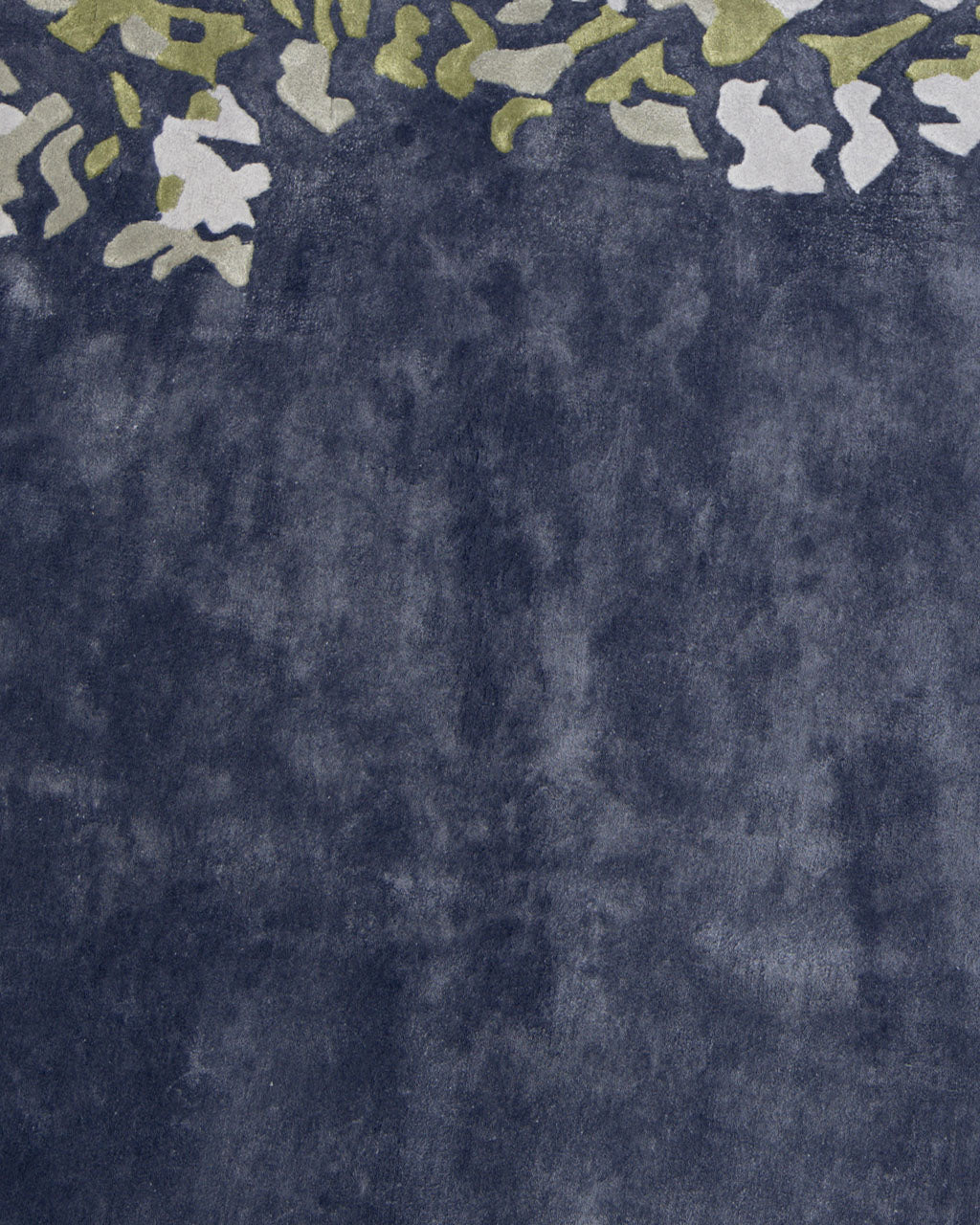 Navy blue textured surface with an abstract pattern of green and white shapes along the top edge, reminiscent of scattered leaves or modern camouflage. The organic design, evocative of a handmade carpet, subtly fades into the solid navy background to create a sophisticated and tactile effect. Product: Navy Blue Viscose Shaped Handmade Carpet 200x300 - HTV-23 by RAMSHA HOME.