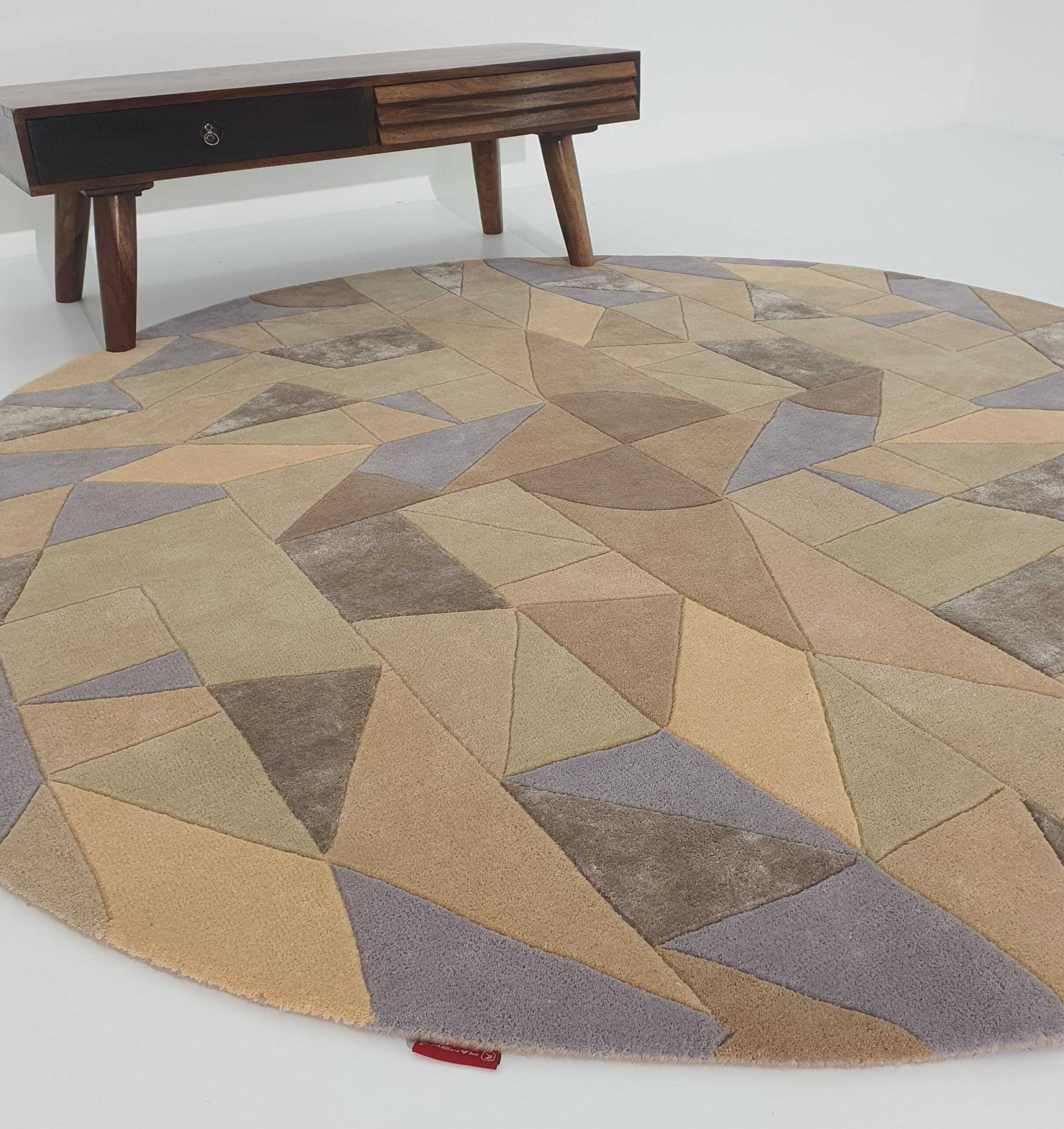 The Vibrant Multi Color Round Handmade Rug - HTWV 50 (200cm) by RAMSHA HOME features a geometric pattern in beige, brown, and gray and is placed on a white floor near a wooden coffee table with angled legs and one drawer.