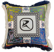 The RAMSHA HOME Polyester Cushion Multi Color CS-058 features multicolored paisley and floral patterns, a checkered border, bold black abstract R in the center, and blue-white fringe trim for a vibrant touch.