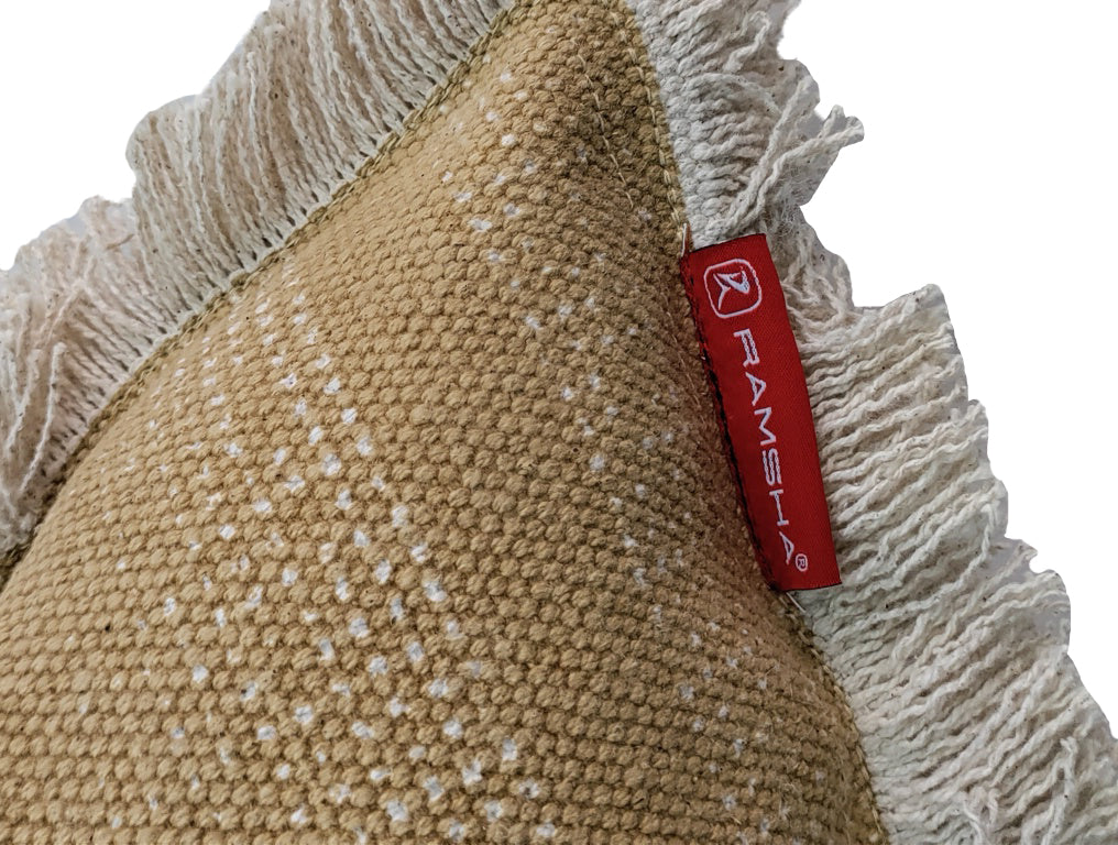 Close-up of the RAMSHA HOME Cotton Cushion With Fringes cs-141, featuring textured beige cotton, white fringe edges, and a red fabric tag labeled RAMSHA® attached to the seam.