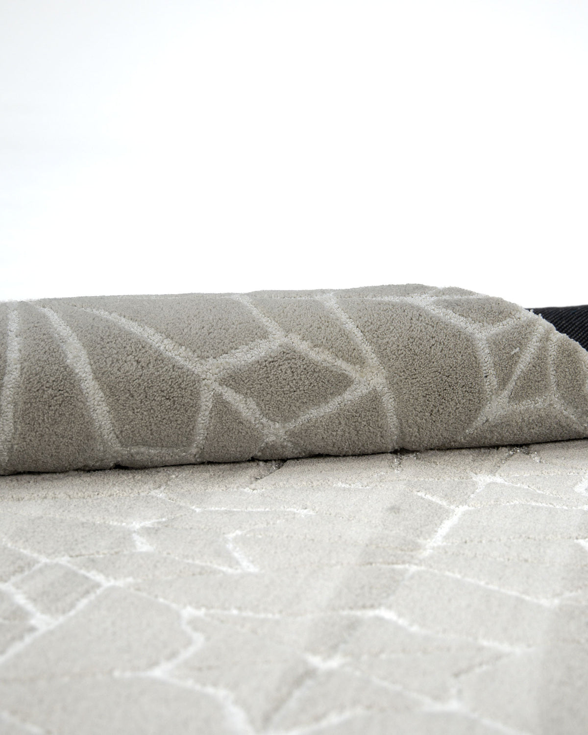 A close-up of the RAMSHA HOME Modern Rectangle Area Rug Multi Color HTP-18, featuring a striking light gray geometric pattern, partially rolled over itself and set against a plain white background.