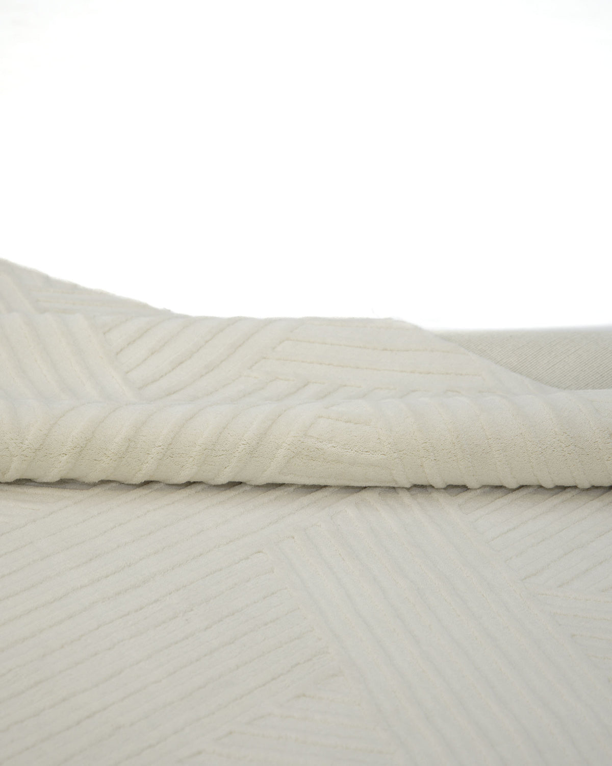 A close-up of the RAMSHA HOME Geometric Woven Natural Color Handmade Area Rug (LKH-016) showcases its folded ivory-hued textured fabric, adorned with a subtle geometric pattern and ridged details. Expertly loom knotted, this area rug artfully blends timeless elegance with modern design, set against a plain white background.