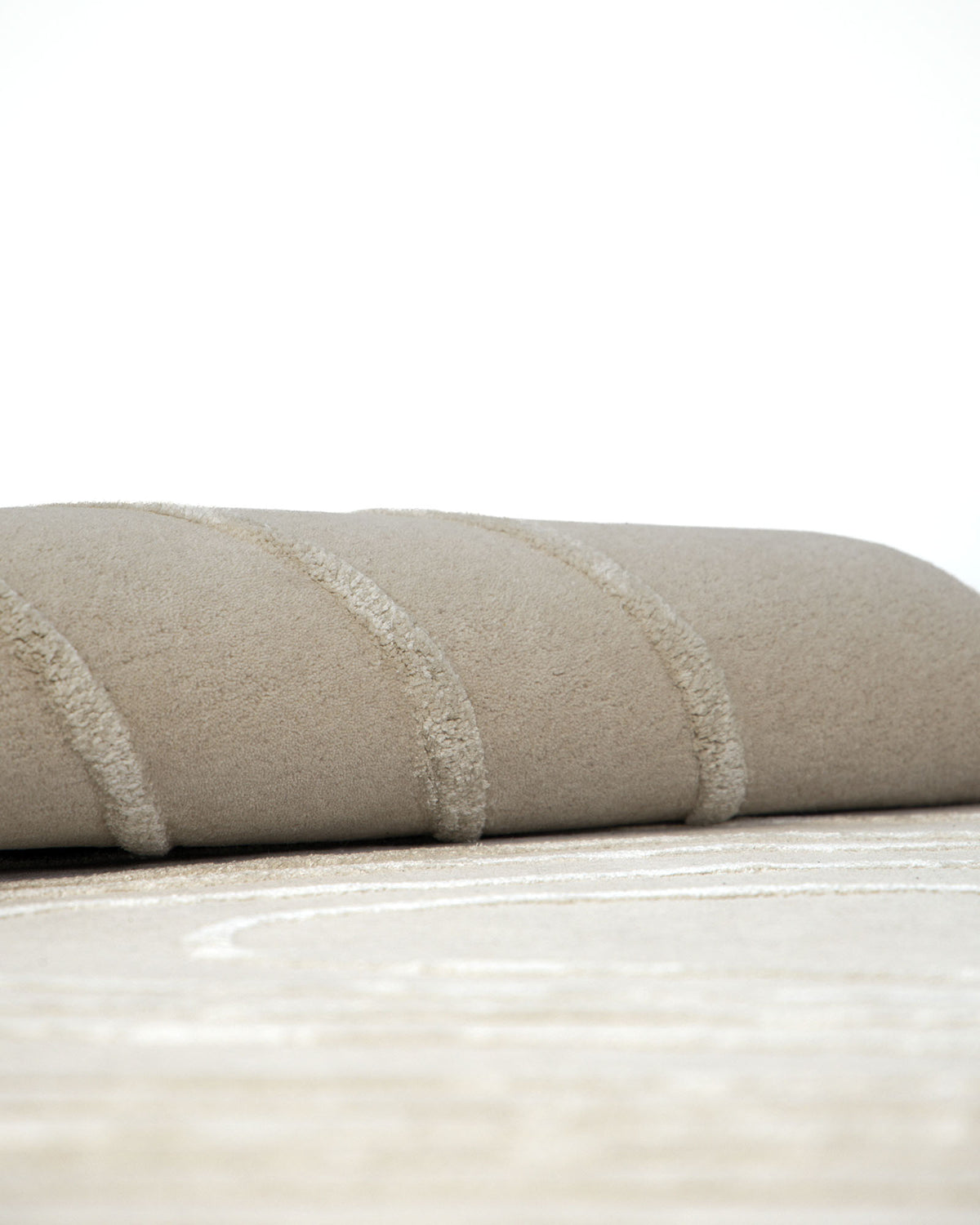 A plush, curved piece of the Luxurious Off-White Wool & Tencel Handmade Area Rug – HTWV 110 (200x300cm) by RAMSHA HOME rests on a matching textured surface, both featuring raised, wavy patterns. The background is plain white.