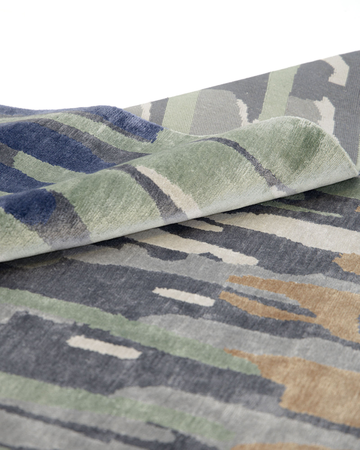 A close-up of the RAMSHA HOME Decorative Area Carpet Tencil & Cotton Multi Color HKV-09, a hand-knotted rug featuring an abstract pattern in green, blue, gray, and beige tones, displayed folded on a white surface.