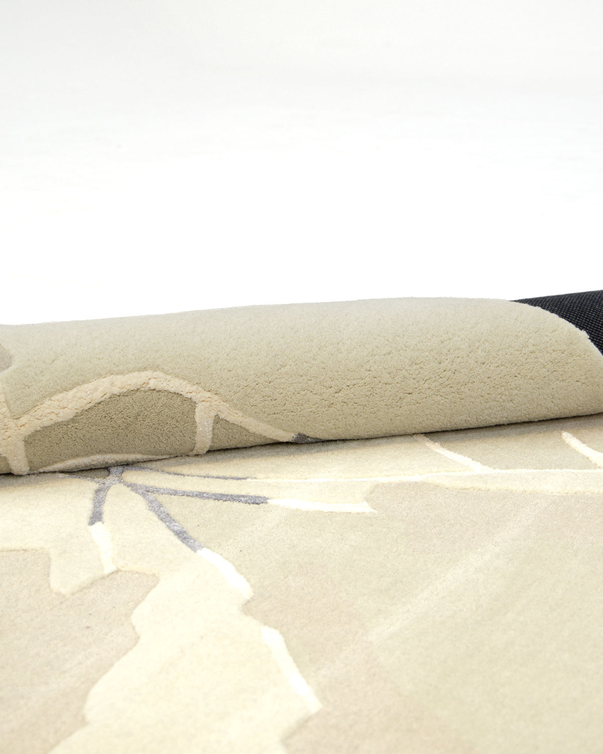 A close-up of the RAMSHA HOME Abstract Multi-Tone Handmade Carpet (HTWV-175, 200x300 cm), featuring a subtle modern design and partially rolled over on a white surface.