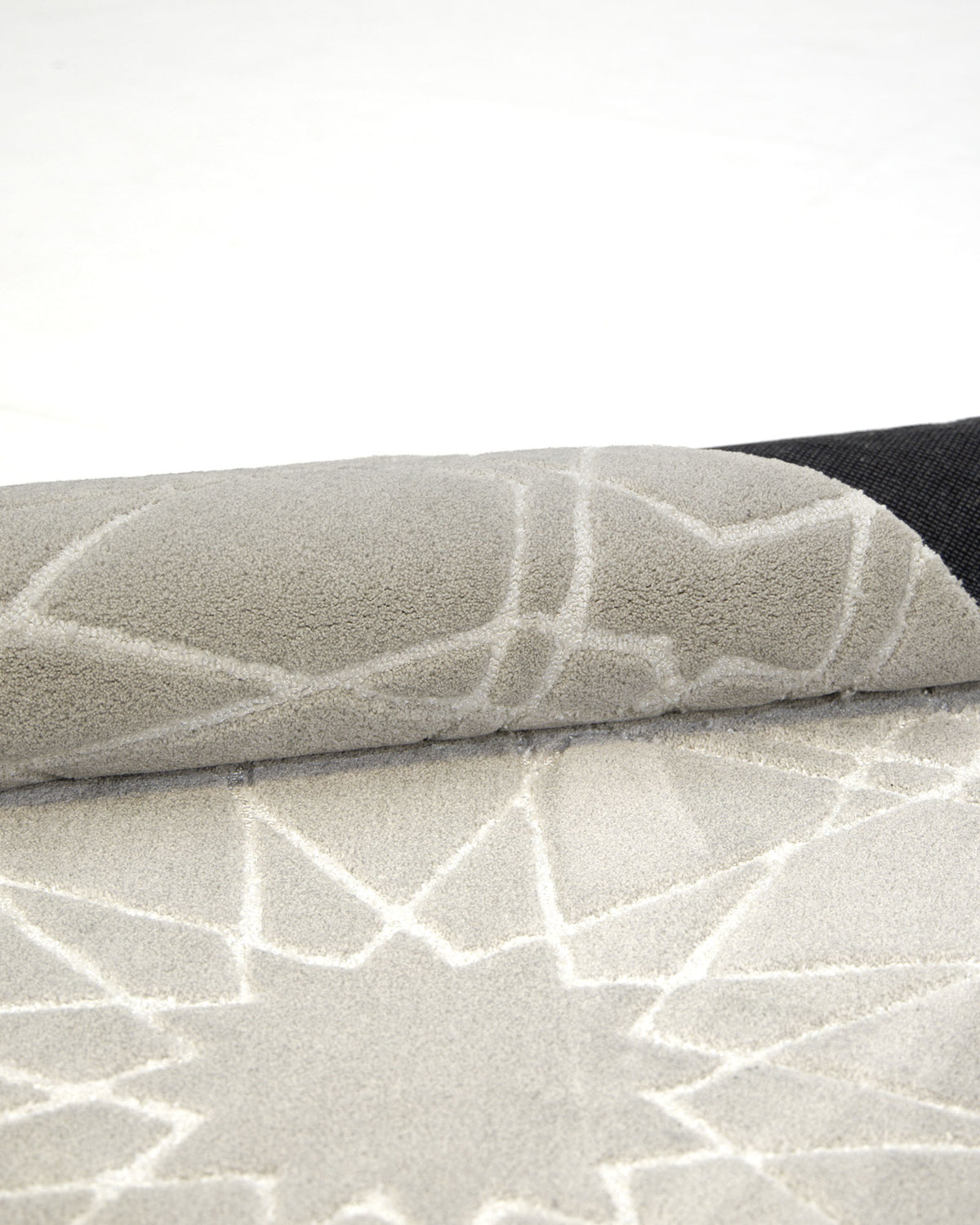 A close-up of the RAMSHA HOME Decorative Rectangle Shape Rug HTP-15, featuring a rolled-up light gray surface with white geometric line patterns, displayed on a white background.
