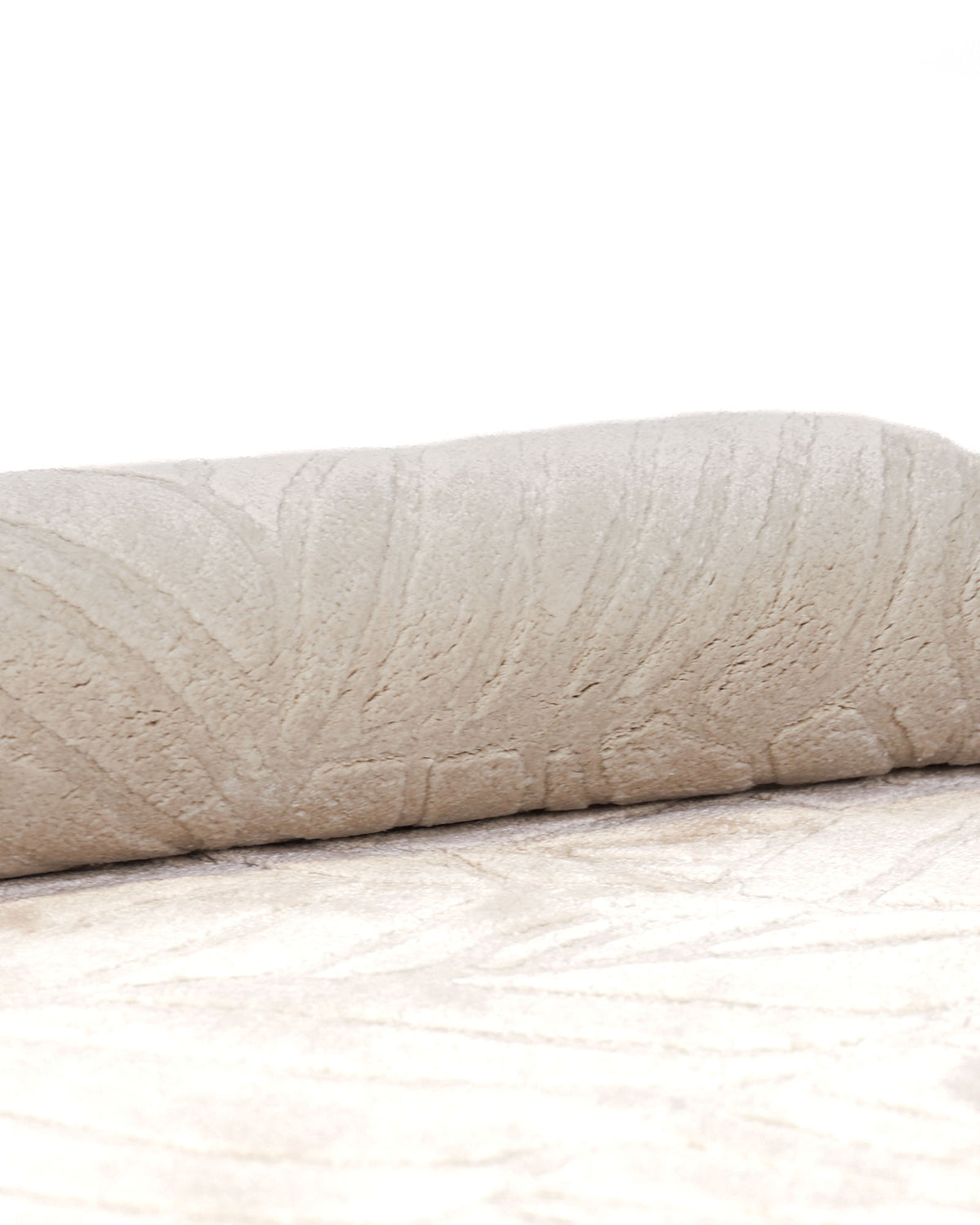Close-up of a rolled-up RAMSHA HOME Rectangle Shape Beige Color Handmade Area Rug - HTV 25 (200x300 cm) resting on a flat surface, both displaying a subtle abstract leaf or branch pattern in neutral tones, reminiscent of textured wallpaper. The background is plain white.