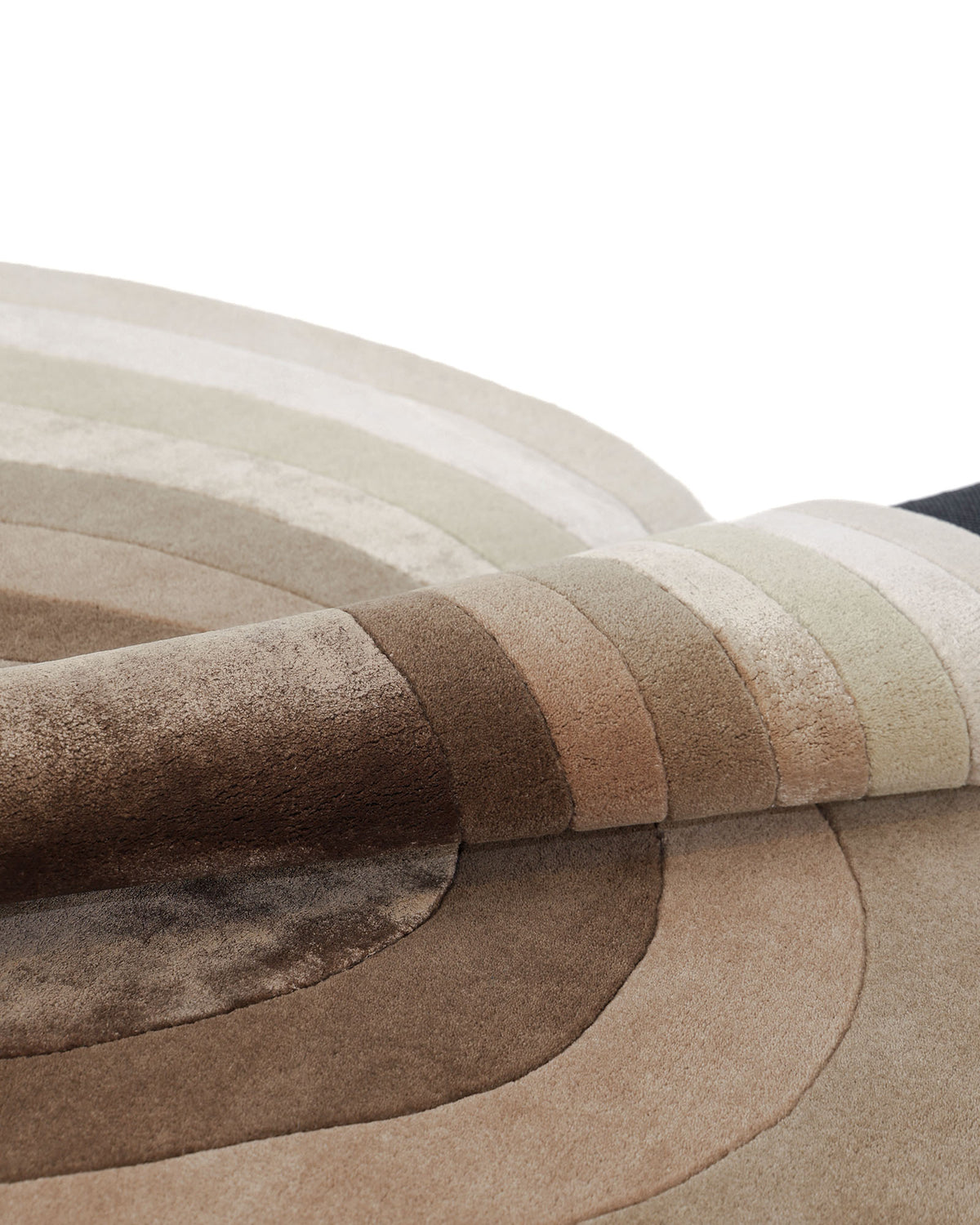 A close-up of the RAMSHA HOME Vibrant Living Room Handmade Rug - HTWV-81 B (200x300cm), featuring textured, hand-tufted wool with curved, concentric stripes in beige, brown, cream, and taupe hues. The corner of this elegant abstract rug is folded over to reveal its plush craftsmanship.