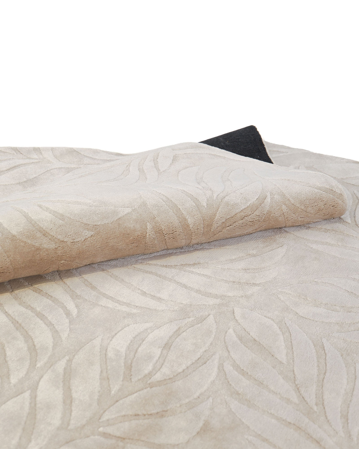 A close-up of the RAMSHA HOME Beige Color Indoor Handmade Area Rug - HTV 15 showcases its raised leaf pattern and partially folded design, revealing a black underside. This hand-tufted rug artfully blends texture and elegance, making it a stylish addition to any space.