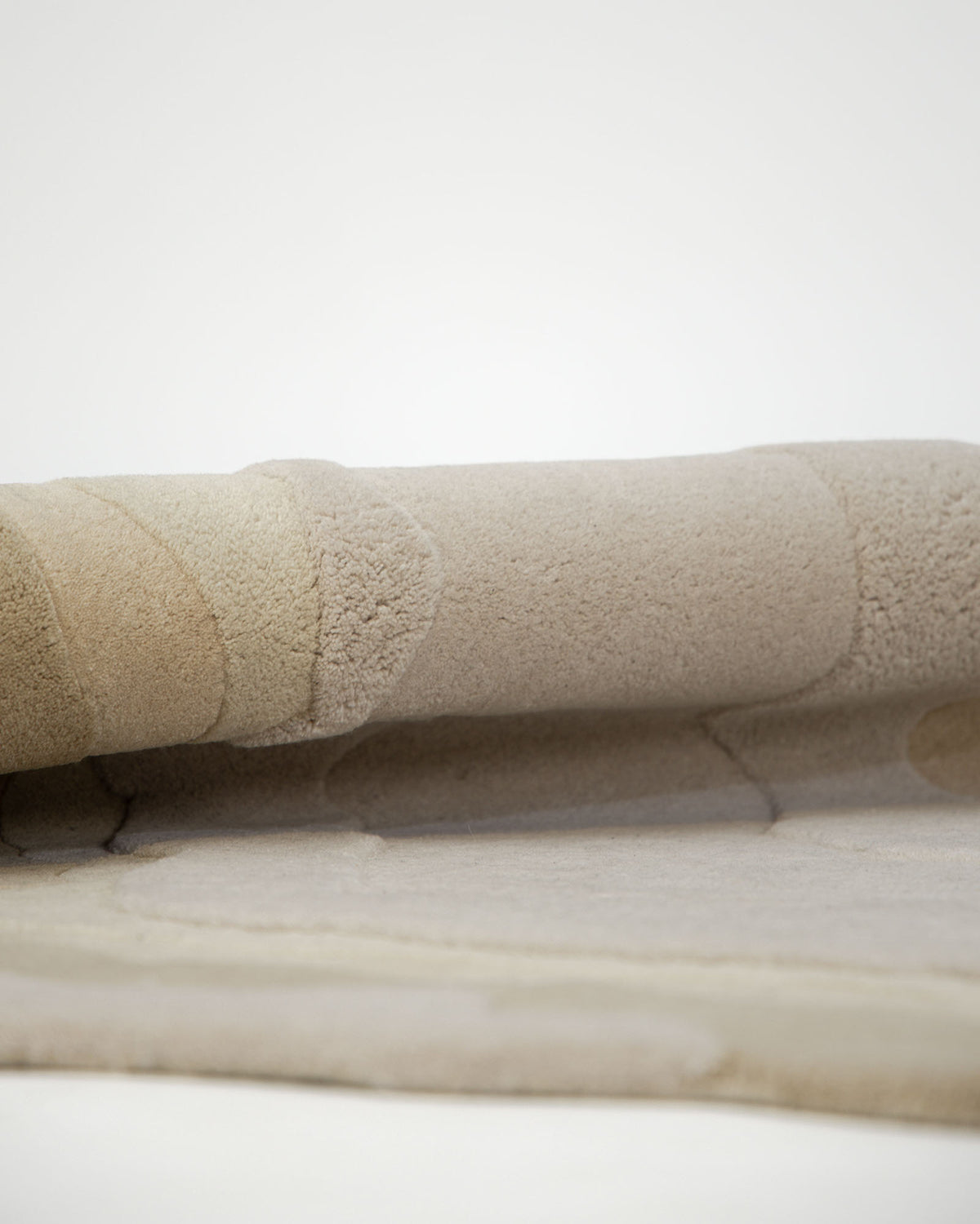 A close-up view of the RAMSHA HOME Contemporary Flow Area Handmade Rug HTW-153, showcasing its folded, textured beige surface with abstract, rounded patterns in various shades of cream and tan on a plain background—perfect for adding a touch of modern interior style.