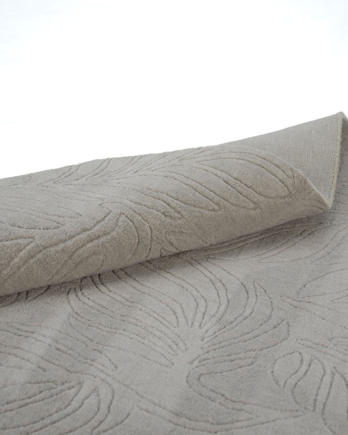 The RAMSHA HOME Decorative Rectangle Handmade Grey Color 200x300 cm Area Rug - LKH-039, featuring a light grey textured surface with a raised abstract leaf pattern, is partially rolled on a white surface.