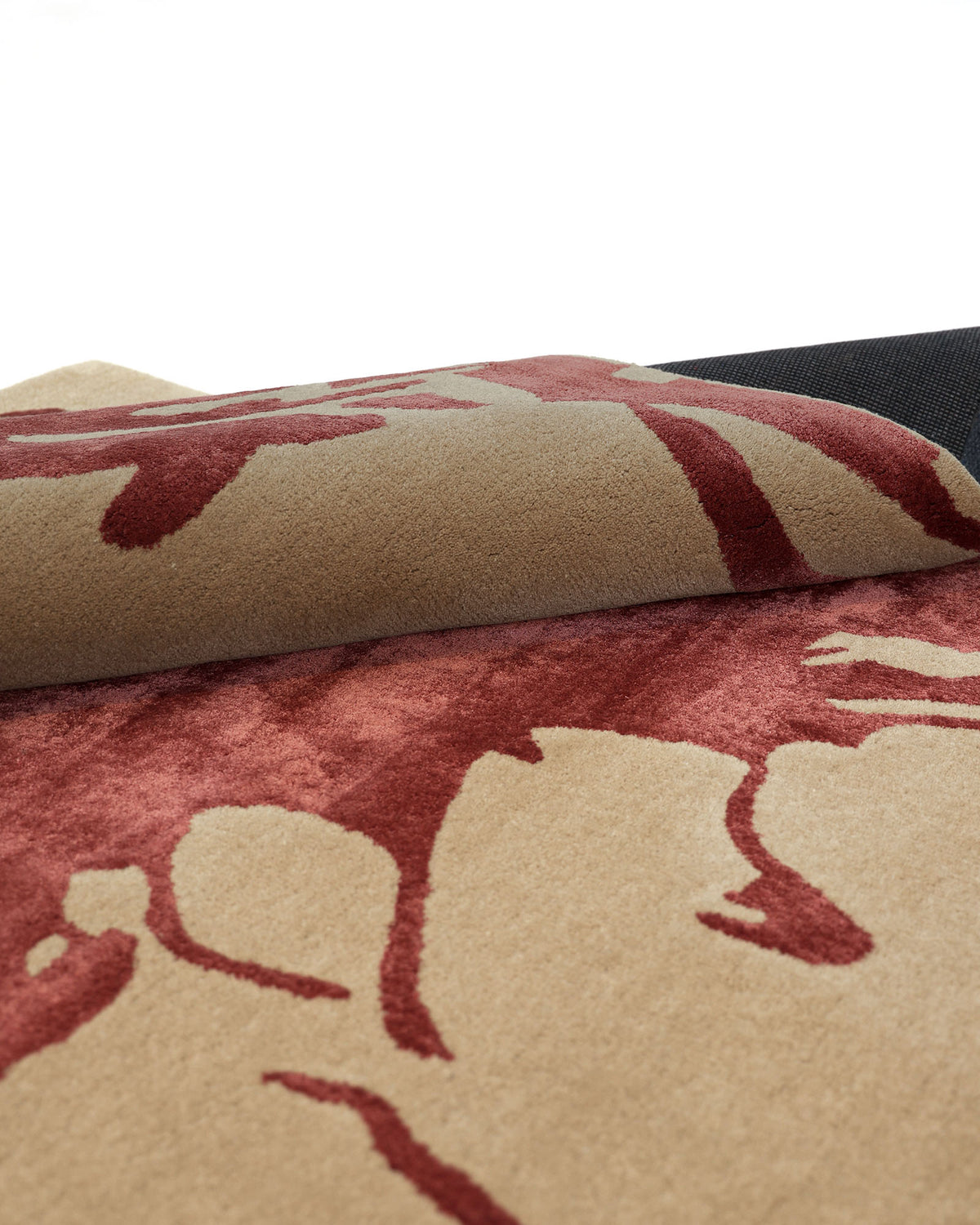 A close-up of the RAMSHA HOME Abstract Burgundy Floral Rug – Modern Artistic Design 153x245 cm (CNZT 16) showcases its beige and red artistic pattern, partially rolled to reveal the dark underside against a white background.