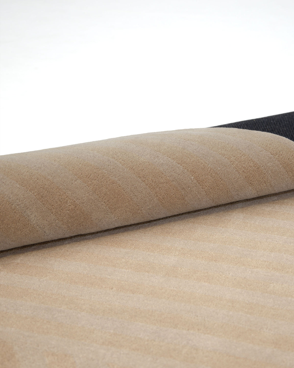A close-up of the RAMSHA HOME Beige Hand Tufted Area Rug 250X350 cm AL-05 reveals its fine craftsmanship, with a subtle striped pattern and elegant texture, partially unrolled on a flat surface—an ideal choice for sophisticated home decor.