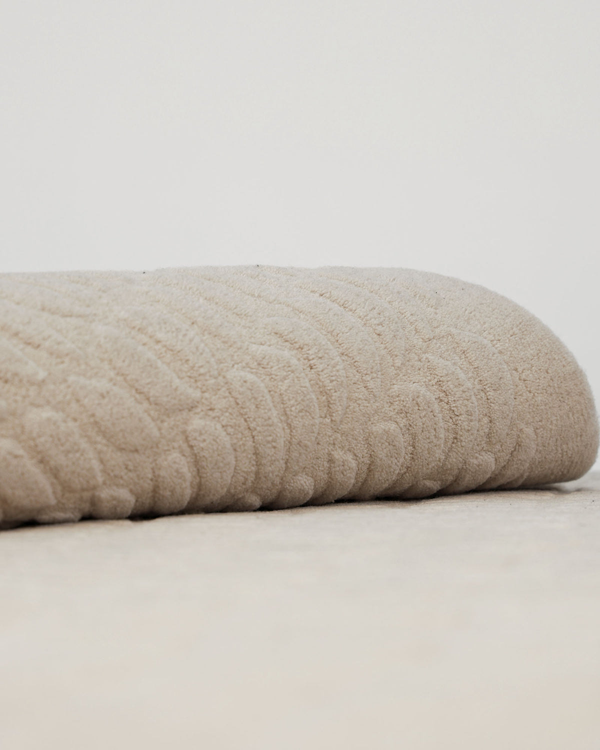 A close-up of the RAMSHA HOME Beige Color Shape Handmade Rug HTW 104 showcases its textured surface and subtle wavy pattern, reminiscent of gentle contours, set against a plain, light background.