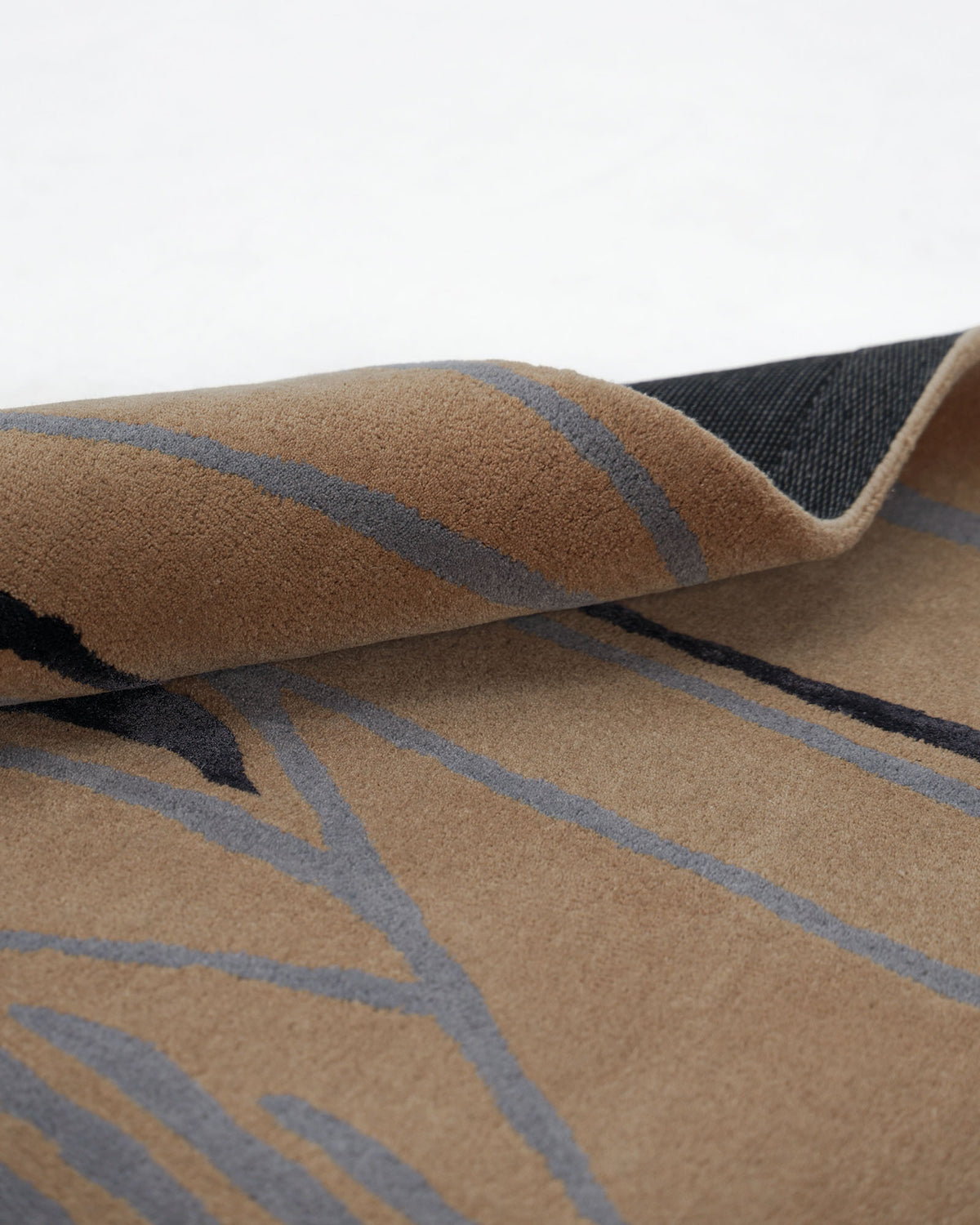 A corner of the RAMSHA HOME Modern Abstract Beige & Blue Line Art Rug – HTWV-25 (202x292 CM) is slightly folded over, revealing its dark underside against a white background.