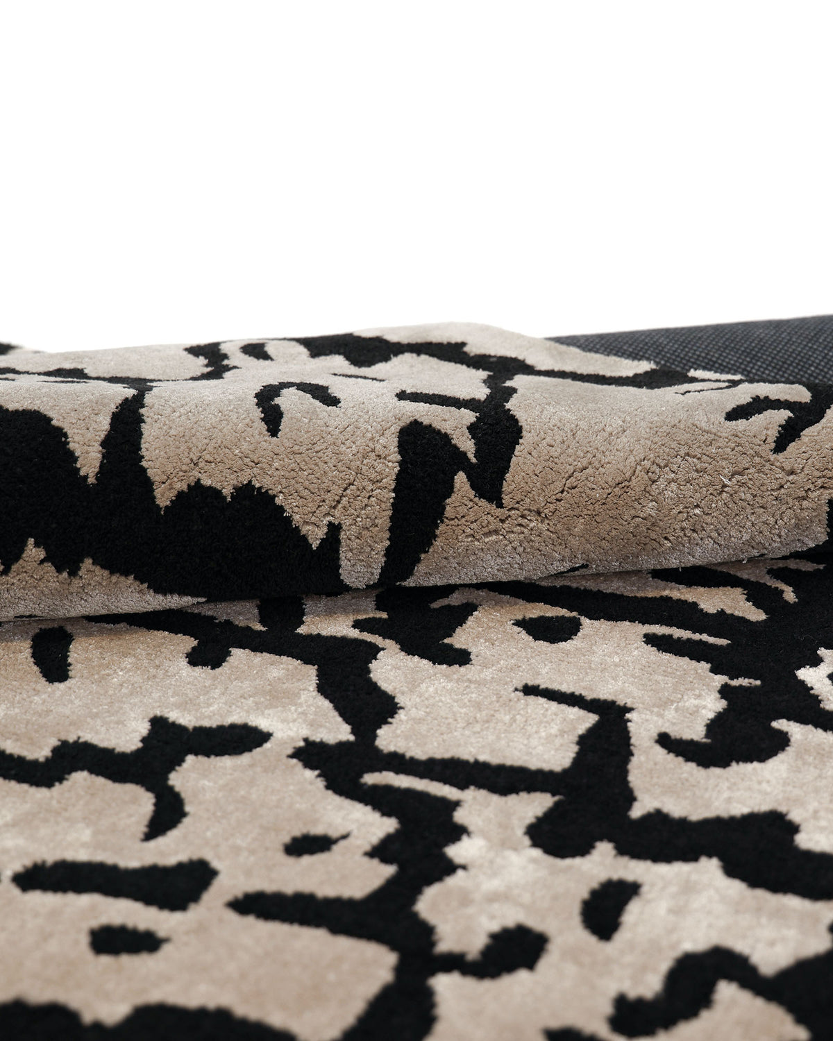 A close-up of the RAMSHA HOME Abstract Crackle Black & Ivory Rug – HTWV-33 showcases its hand-tufted, soft and plush texture in beige and black, highlighted by a bold abstract jagged pattern. Part of the rug’s underside is also visible.
