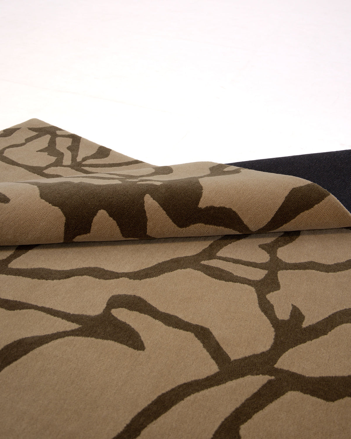 A close-up of the Stunning Multi Color Fluffy Wool Handmade Rug - HTW 21 (202x292cm) by RAMSHA HOME showcases its hand-tufted texture and thickness, with a dark abstract, branch-like pattern partially folded over against a light background.