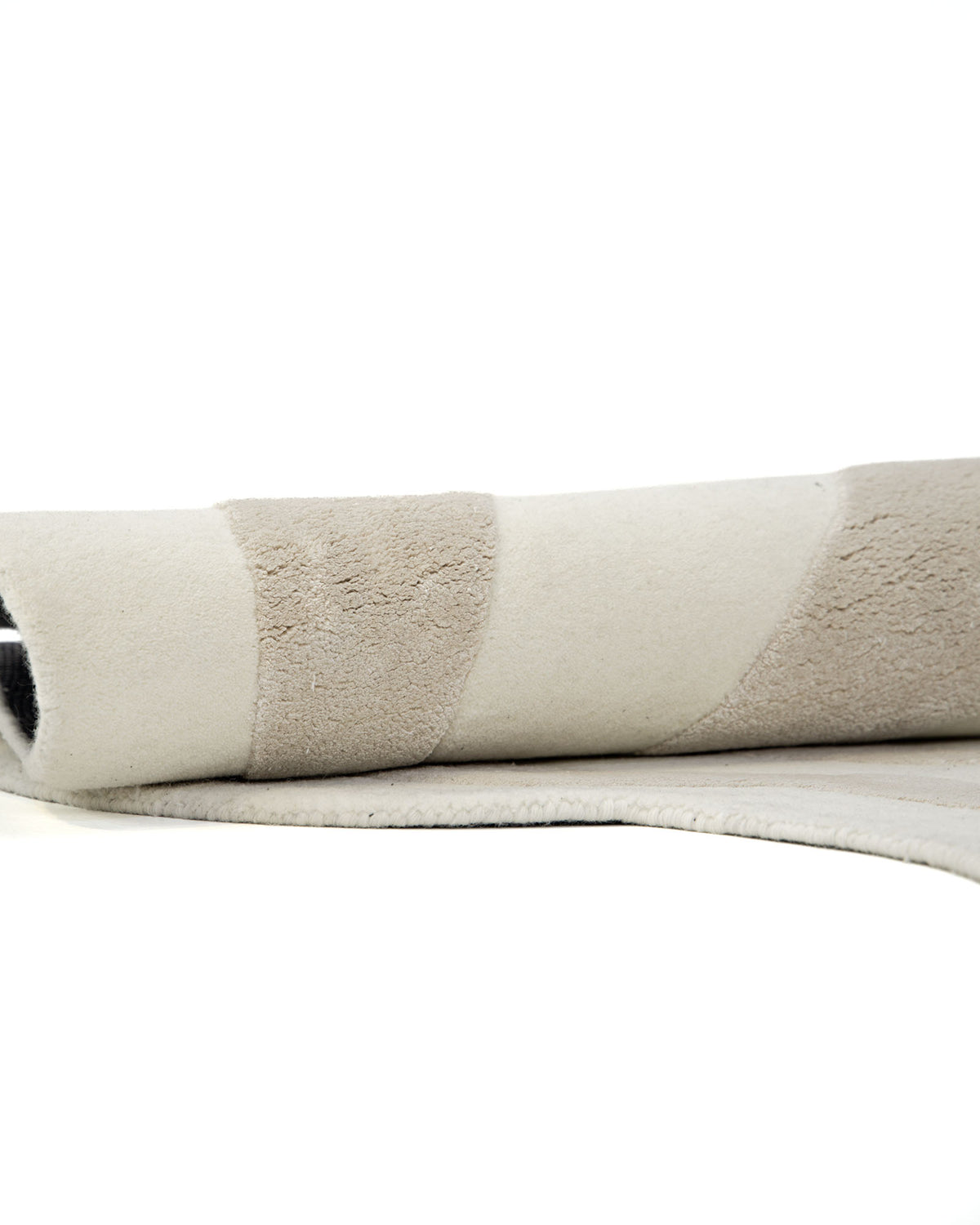 A close-up of the RAMSHA HOME Beige & Cream Wavy Handmade Area Rug – HTWV-144, showcasing its neutral curved and wavy pattern in beige and cream tones. The hand-tufted viscose rug is partially rolled and displayed on a white surface.