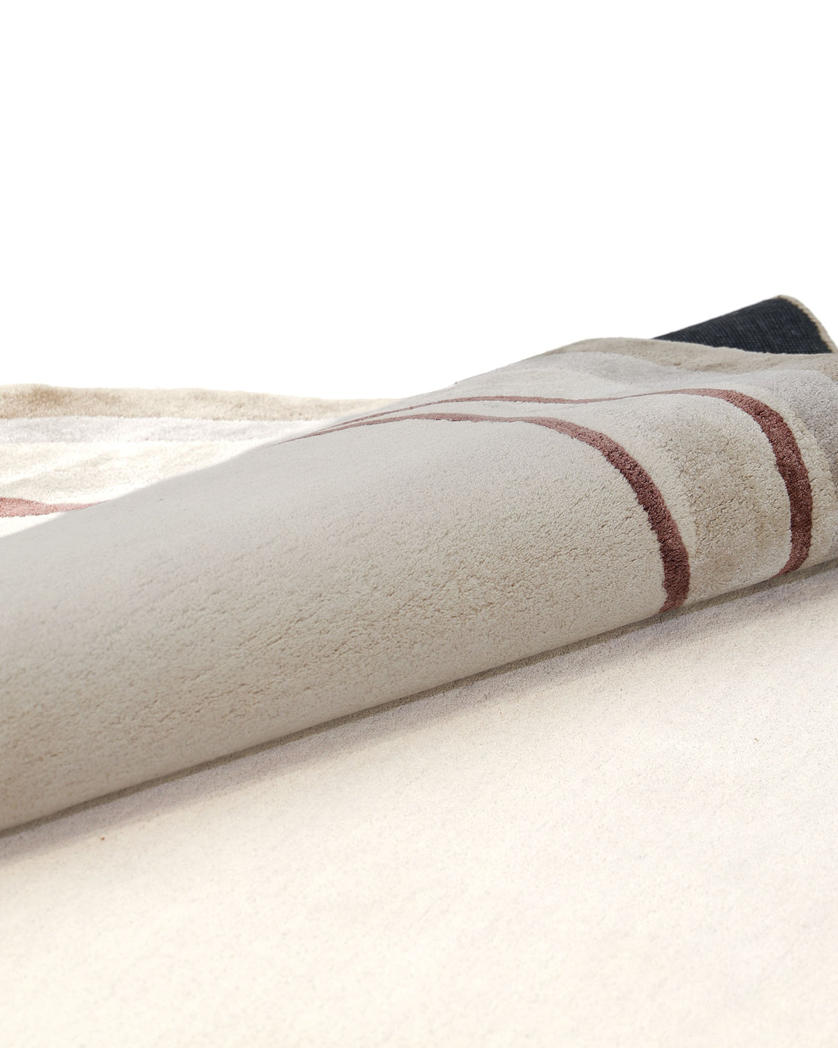 A Handmade Hand-Tufted Carpet HTWV-60 by RAMSHA HOME in beige with brown lines is partially rolled up on a flat surface, revealing both the front and back sides of this artisan-made rug.