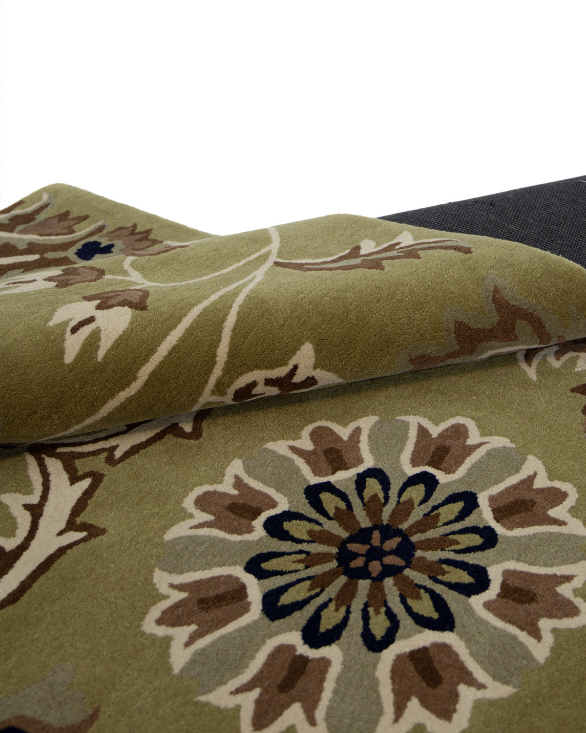 A close-up of the RAMSHA HOME Home Decor Multi Color Handmade Rug - HTW 10 (200x300 cm) showcases its green floral-patterned, hand-tufted wool surface, partially folded to display the backing. The traditional area rug design features flowers in shades of brown, beige, blue, and cream intertwined with elegant curving vines.